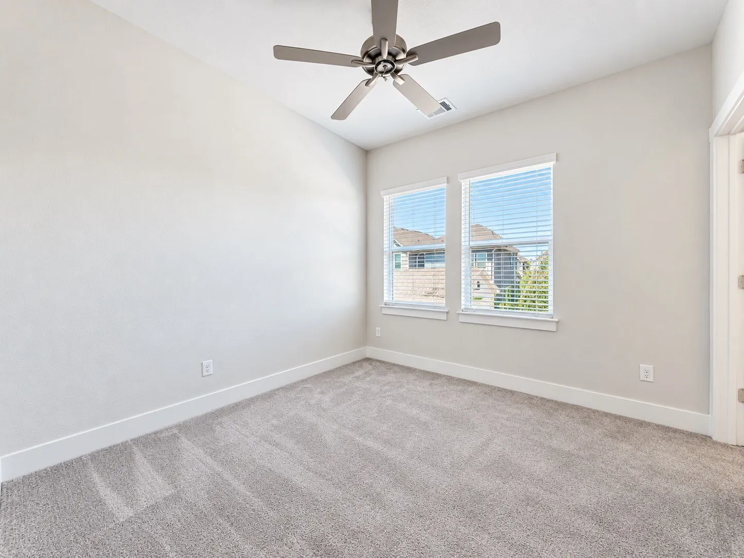 Vaulted ceiling with a ceiling fan, two windows with blinds, and light-colored carpet