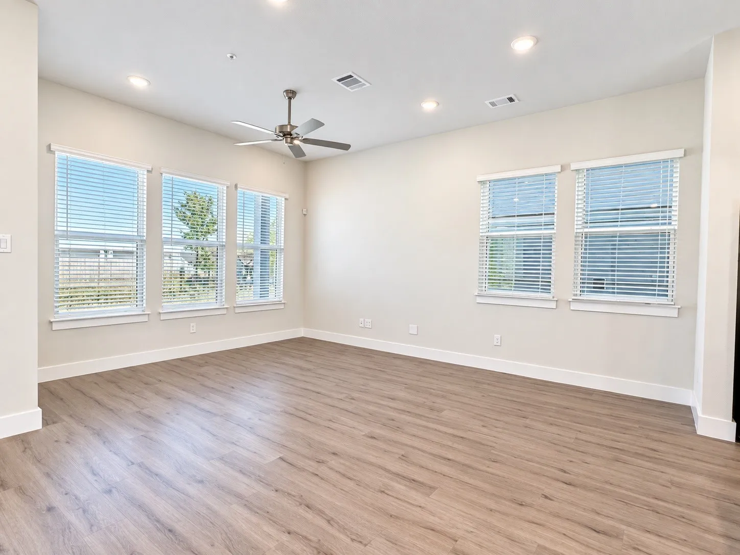 Spacious room featuring wood-finish flooring, multiple windows with blinds, recessed lighting, and a ceiling fan