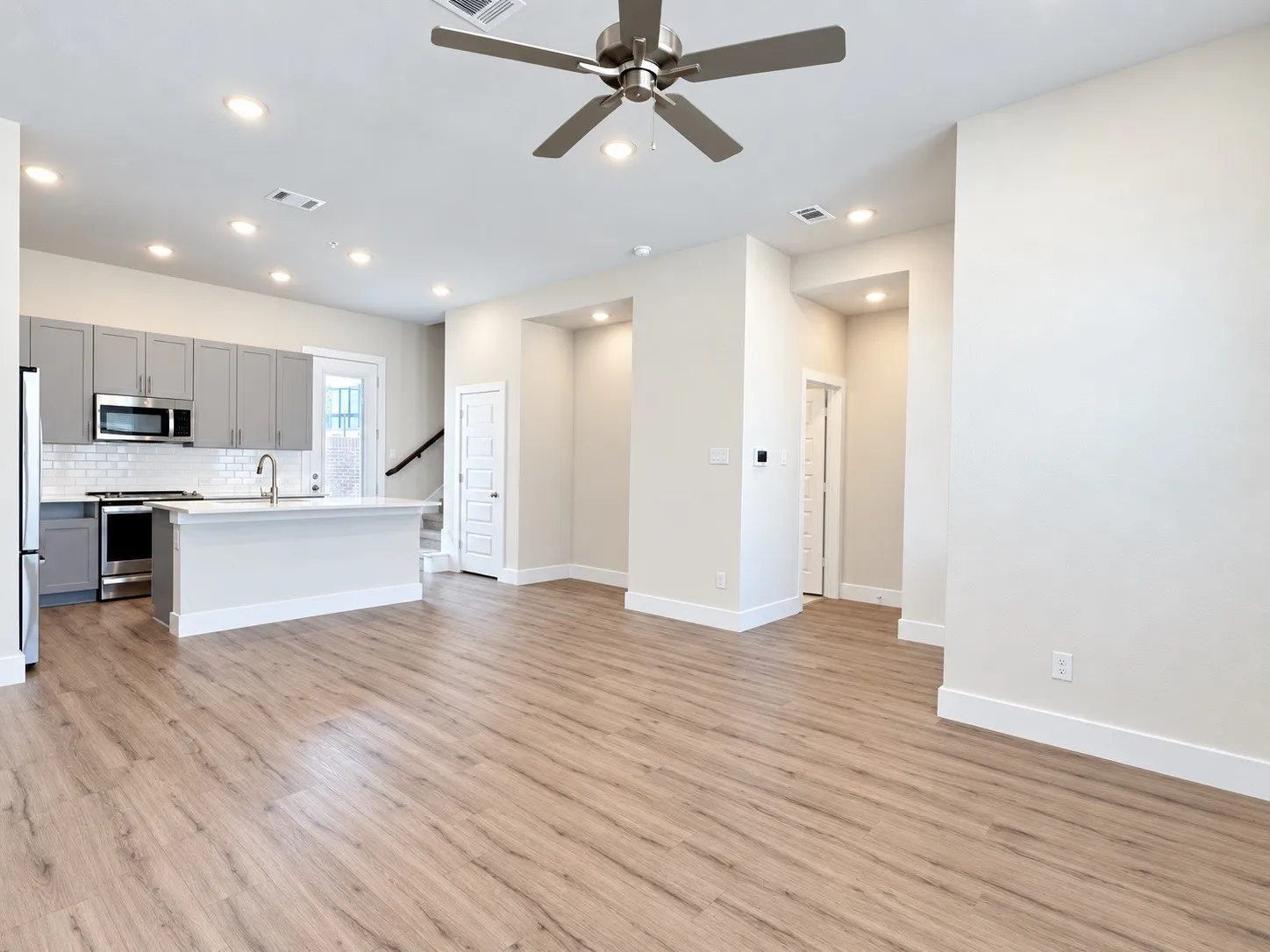 Open-concept living area featuring wood-finish flooring, recessed lighting, a ceiling fan, and a kitchen with gray cabinetry and stainless steel appliances