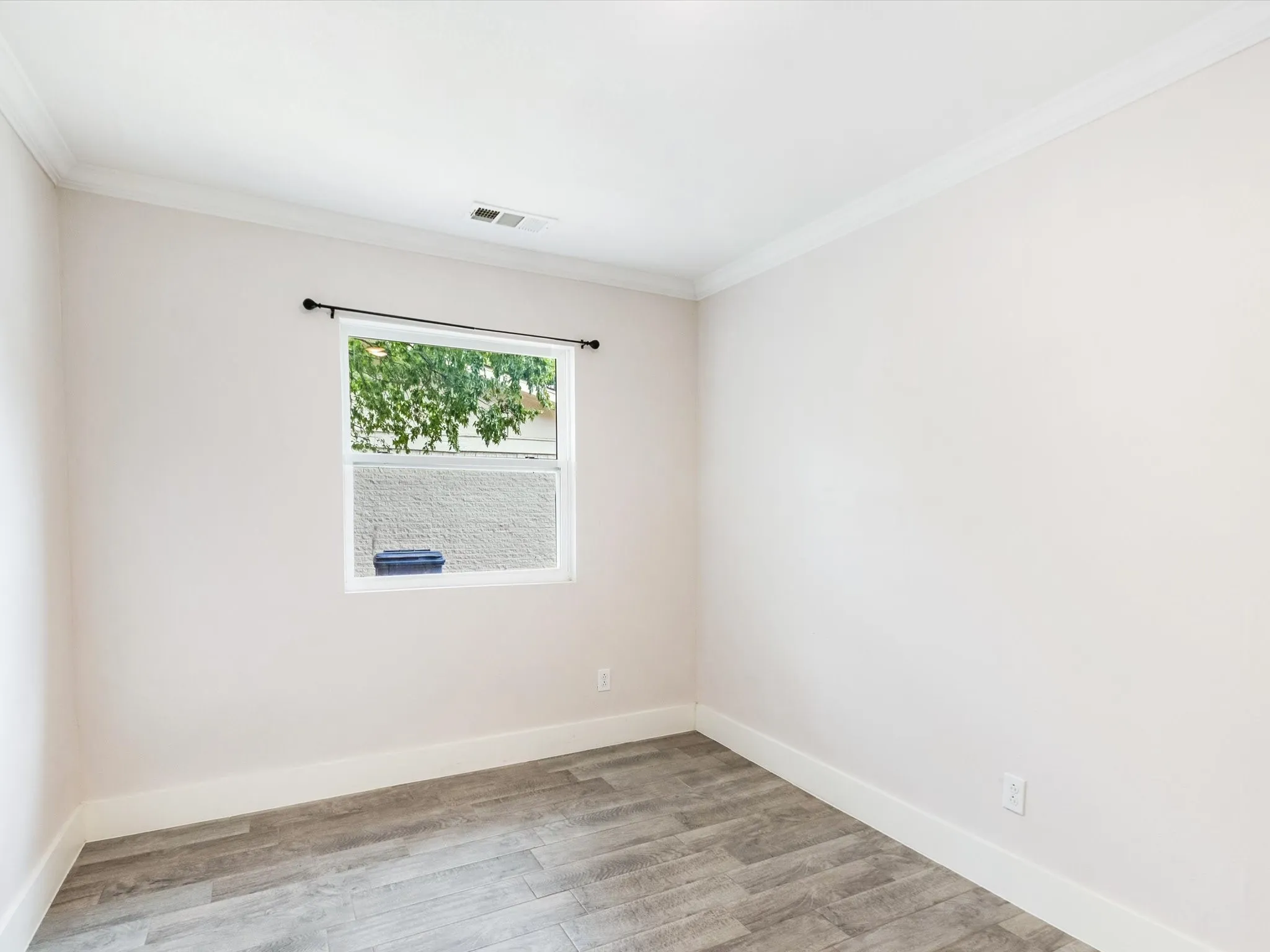 Light-filled room featuring wood-finish flooring, a single window, and crown molding