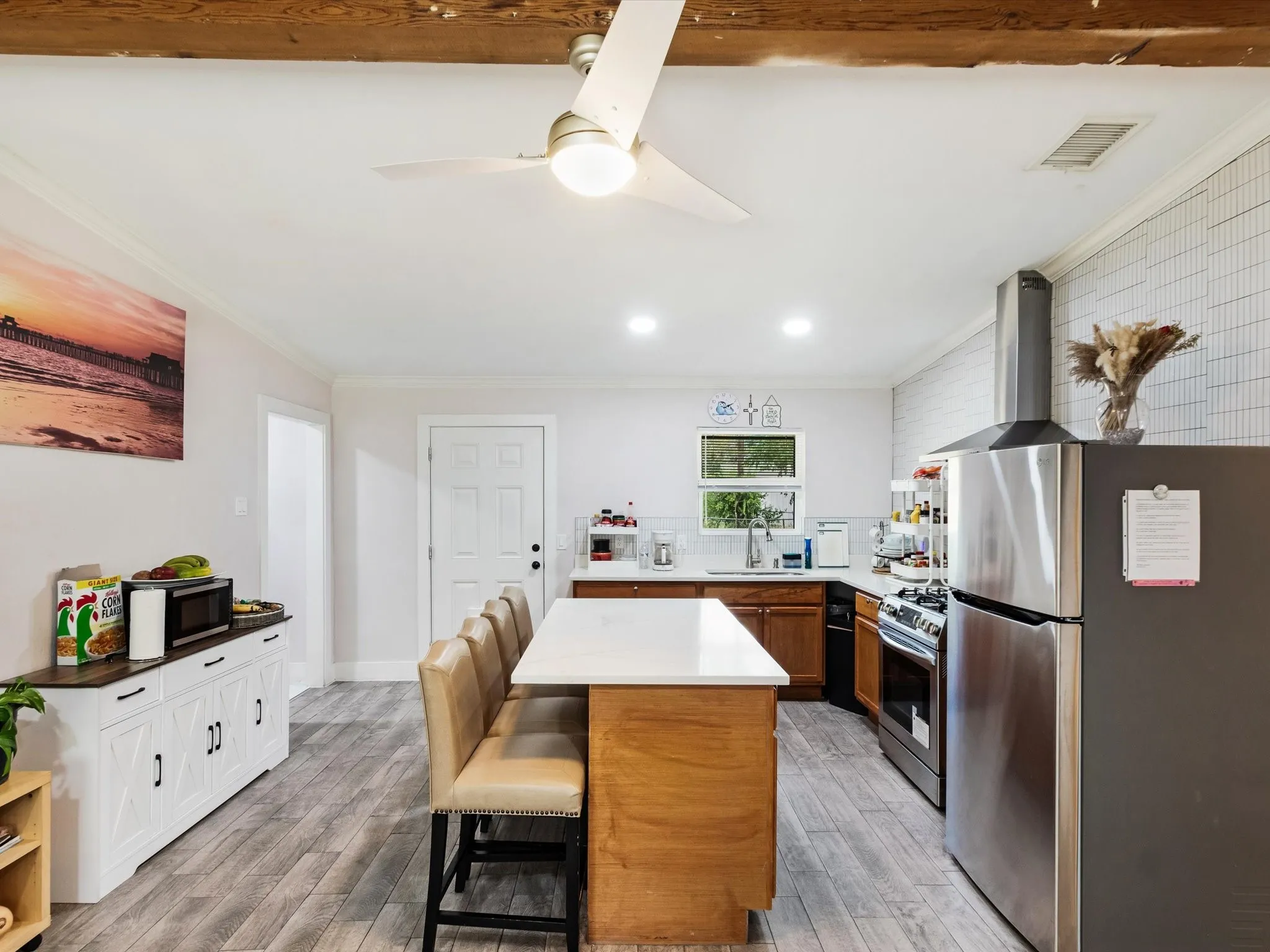 Kitchen featuring wood-finish flooring, an island with countertop seating, stainless steel appliances, and a tiled backsplash
