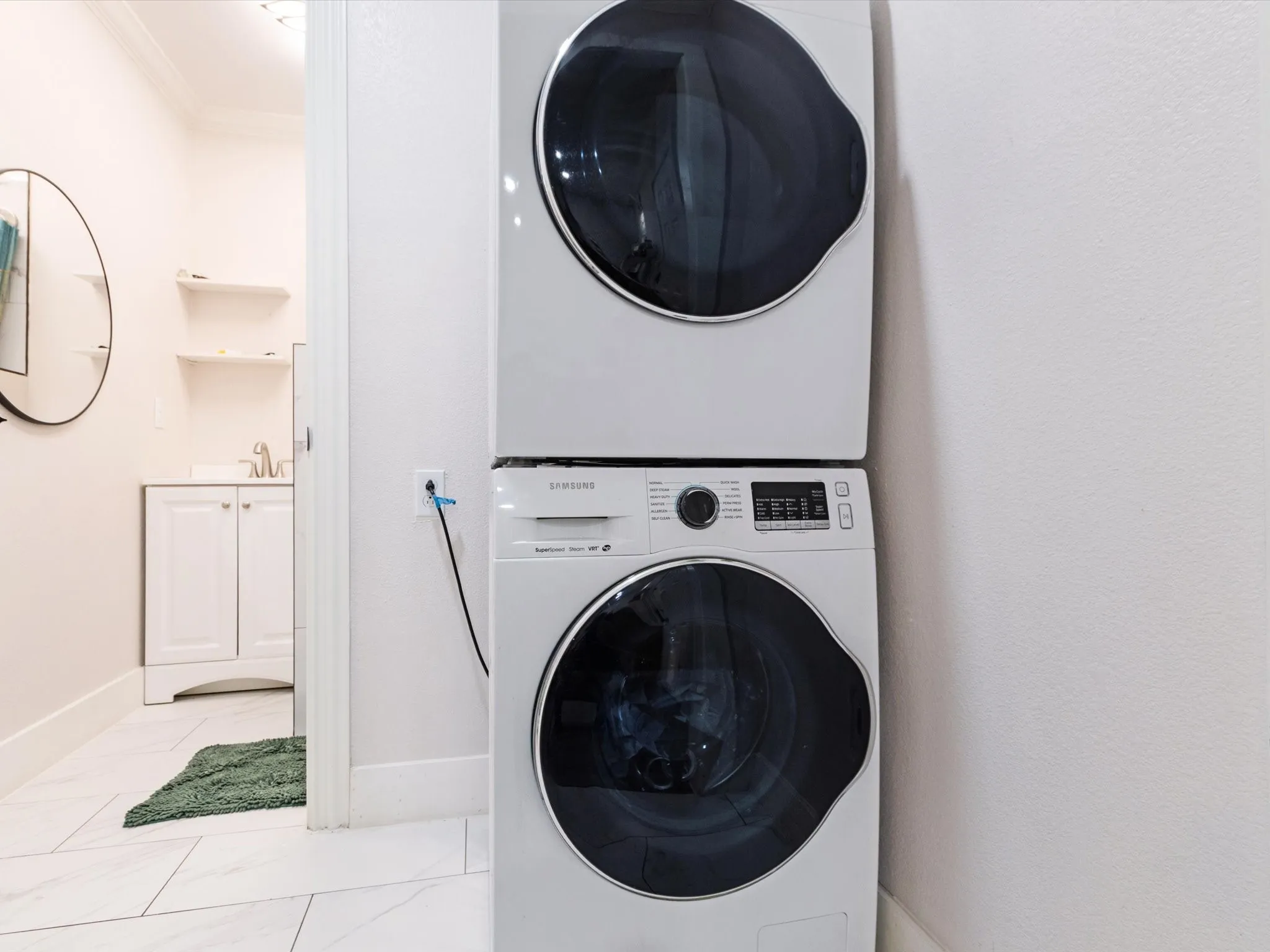 Stackable washer and dryer, white cabinets, white tile flooring, and wall-mounted shelving