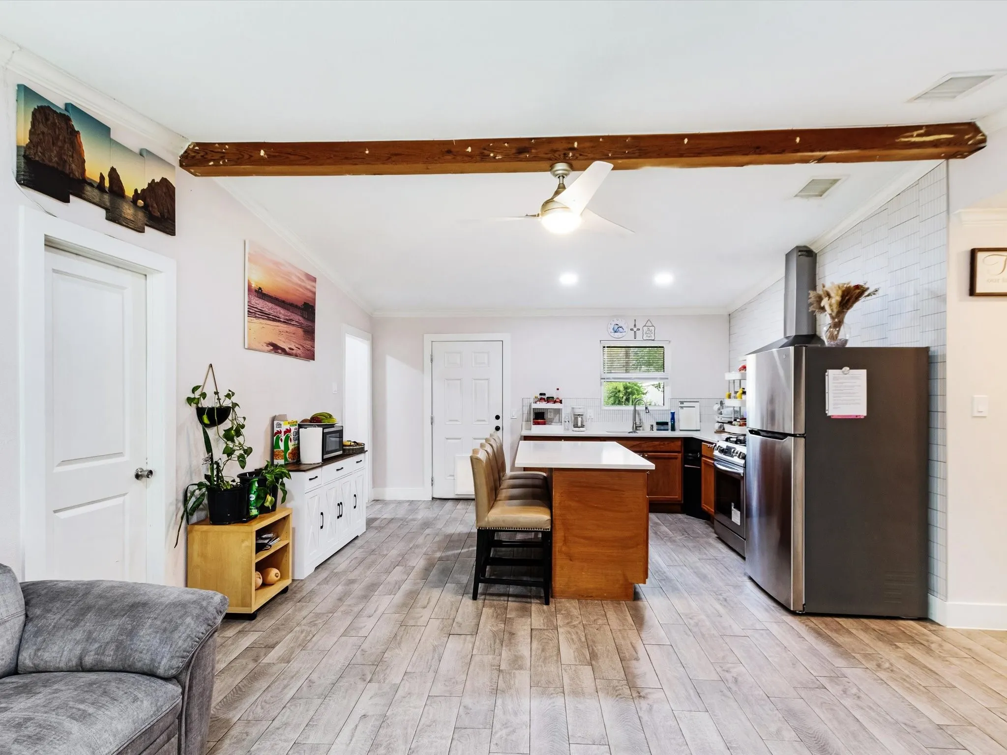 Open-concept living space with wood-finish flooring, exposed ceiling beam, recessed lighting, and a contemporary ceiling fan