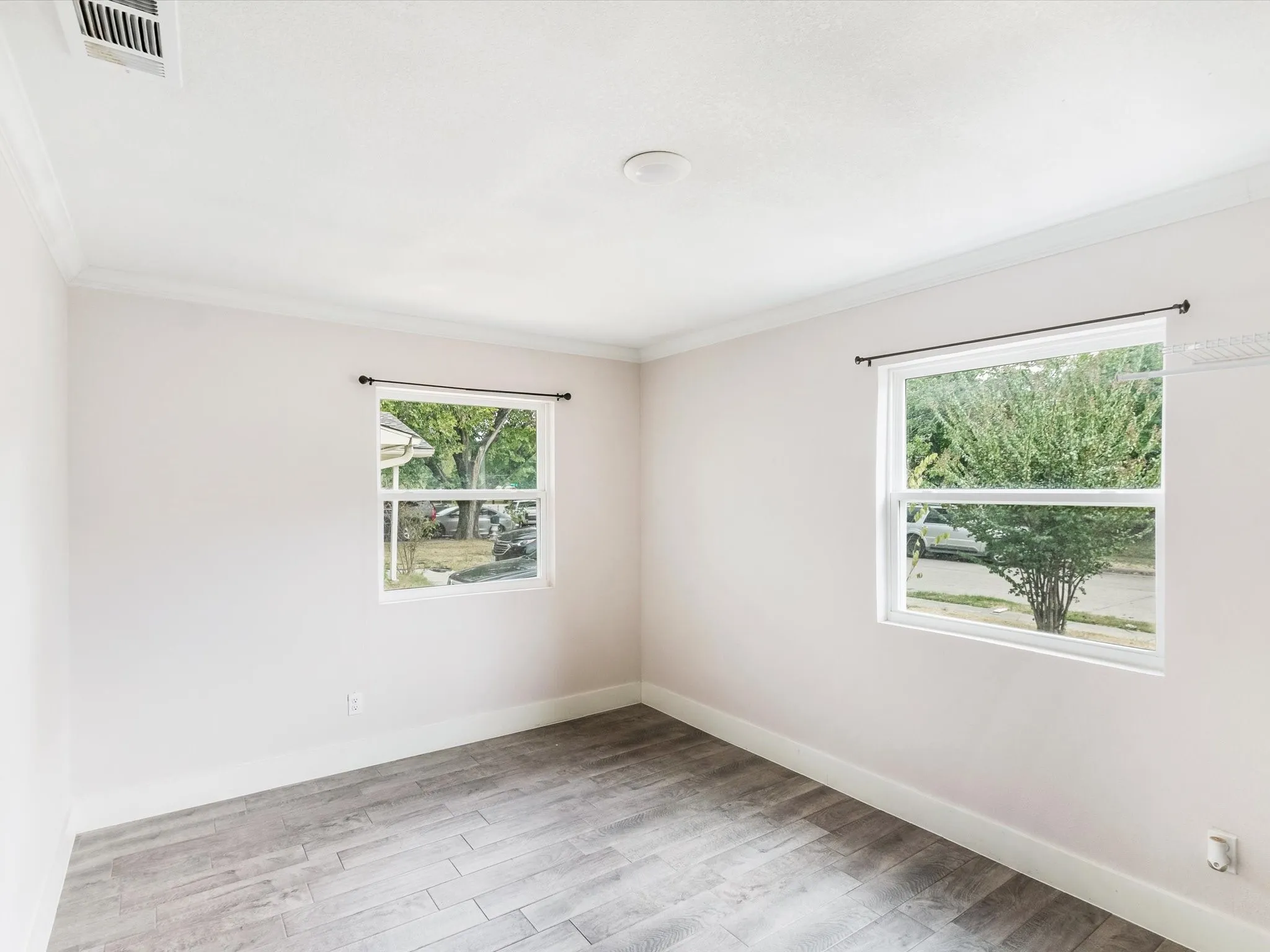 Wood-finish flooring, two large windows, crown molding, and a ceiling-mounted light fixture