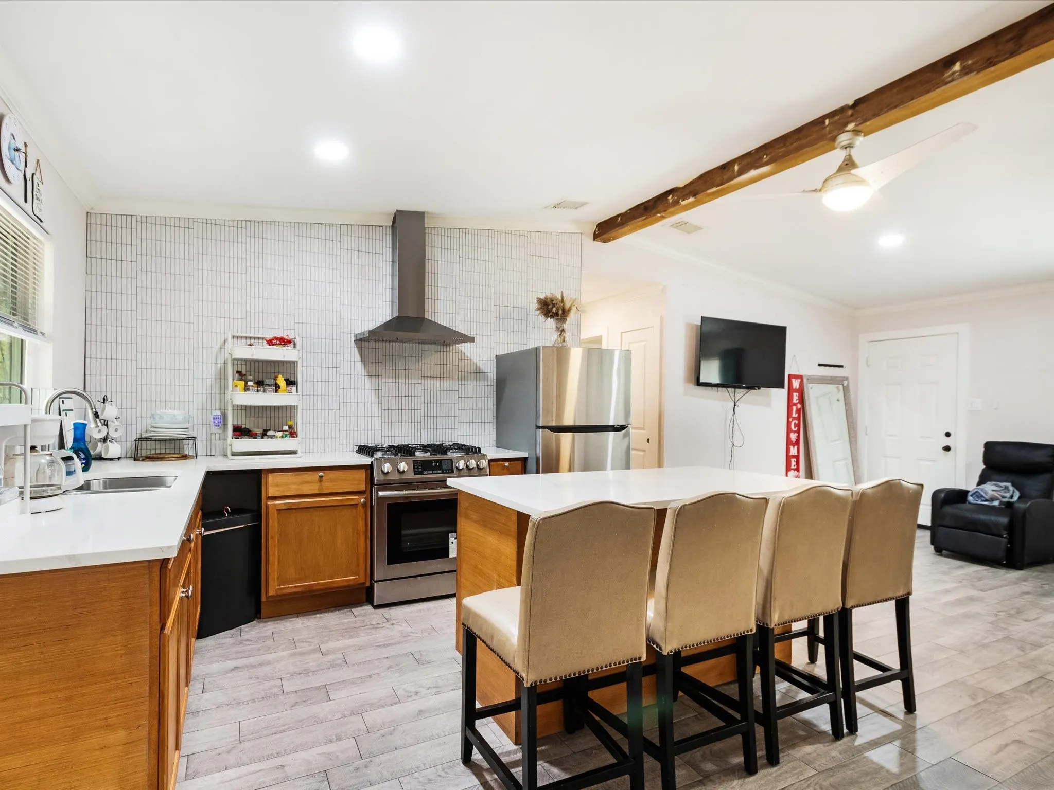 Kitchen featuring stainless steel appliances, a tile backsplash, light wood-finish cabinetry, a central island with bar seating, and wood-look flooring