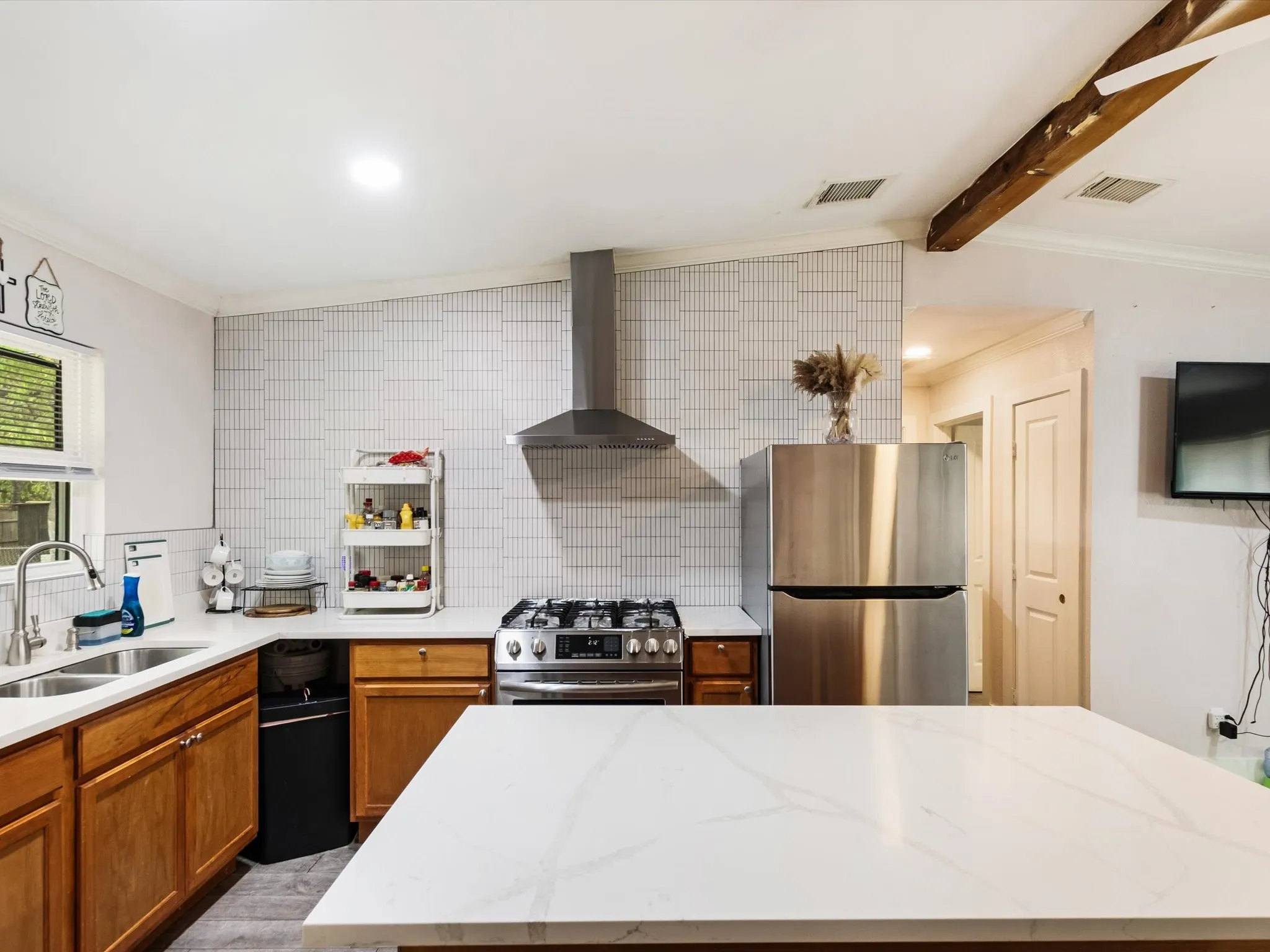 Modern kitchen featuring stainless steel appliances, a gas range with a range hood, and light-toned cabinetry