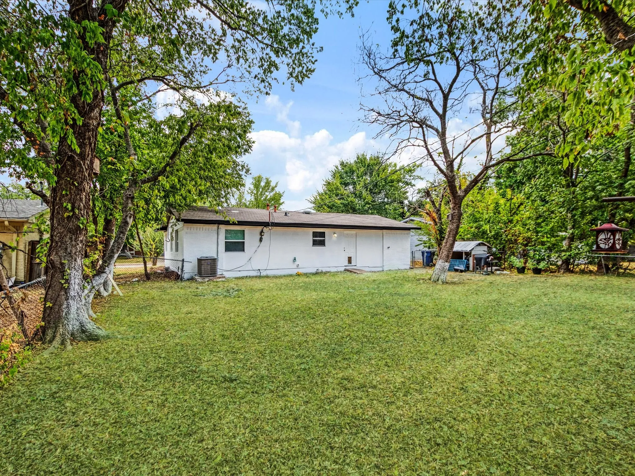 Expansive green space featuring a white exterior structure with a dark roofline, mature trees, and an air conditioning unit