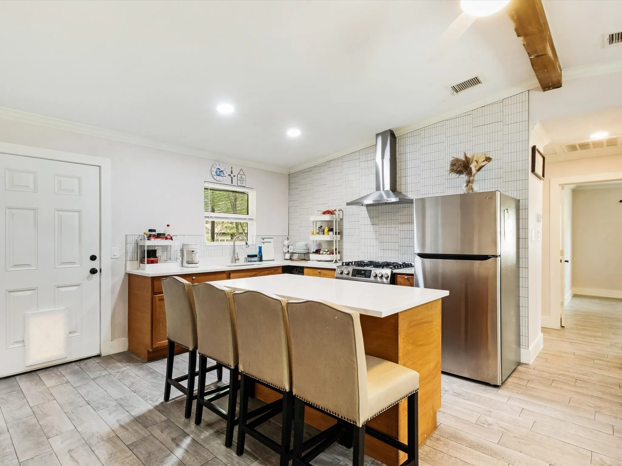 Wood-finish flooring throughout, complemented by a white subway tile backsplash, stainless steel appliances, and a wood beam ceiling accent