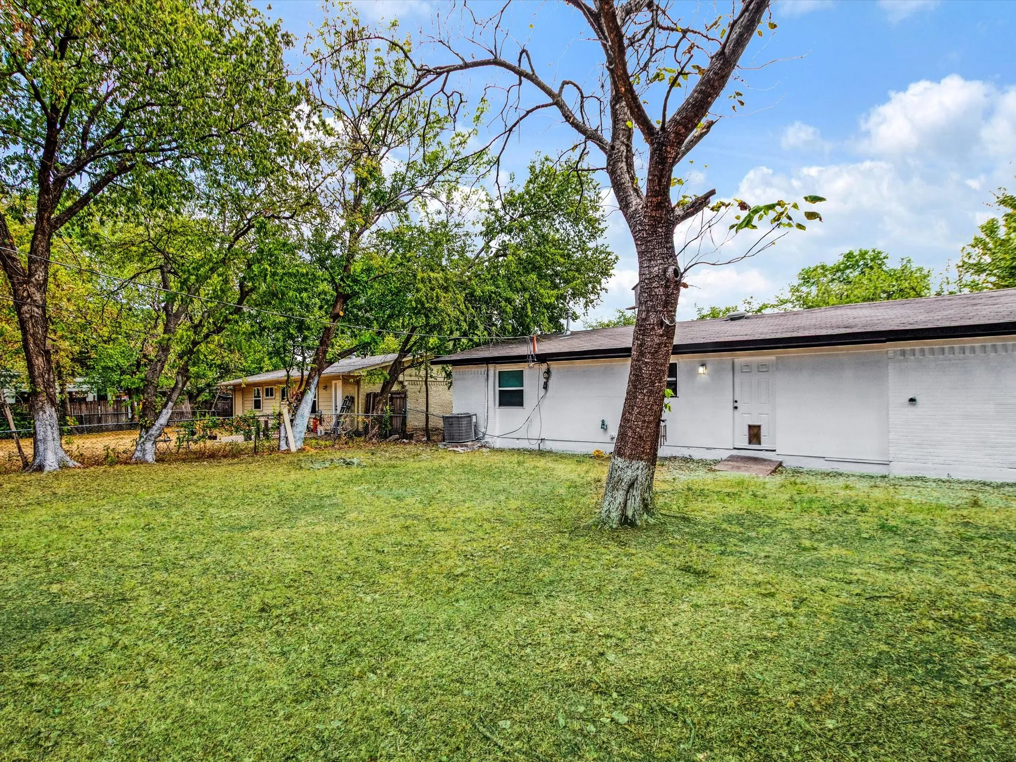 Expansive green lawn with mature trees, featuring a white painted brick exterior and dark roofline