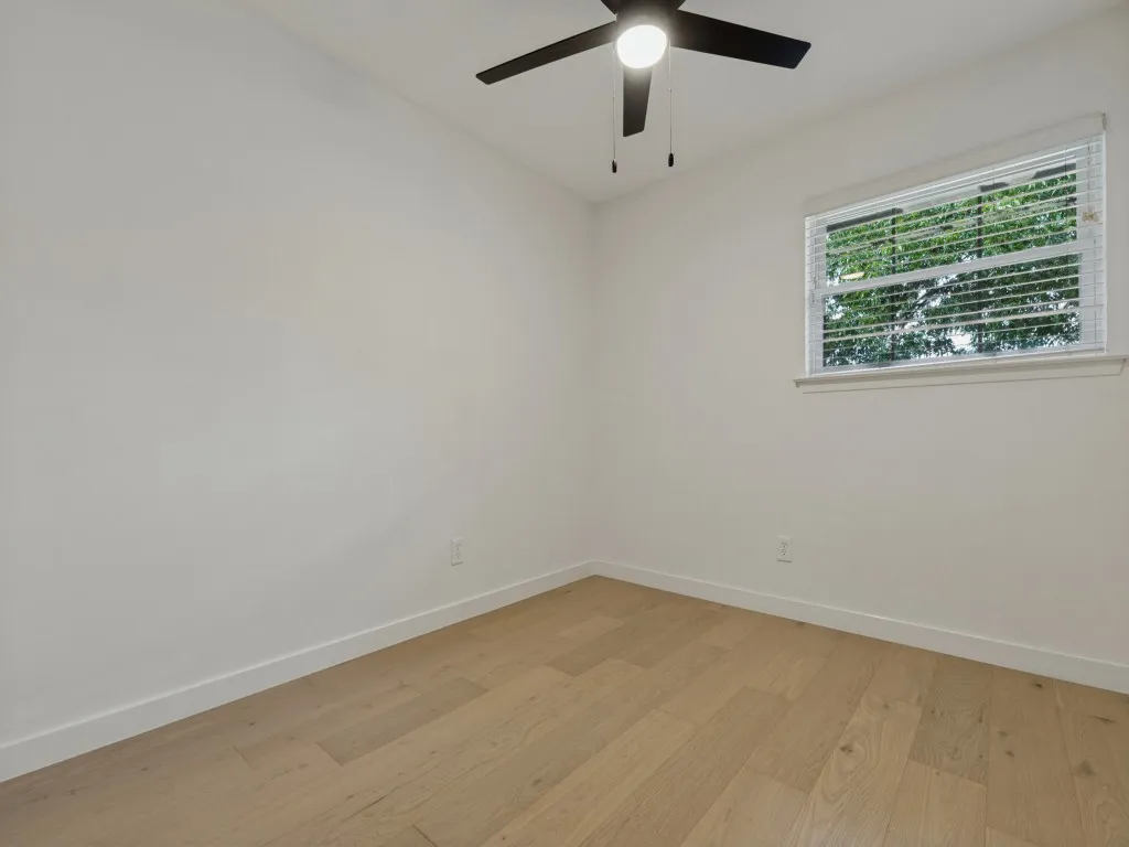 Light wood-finish flooring with white baseboards, a window featuring blinds, a ceiling fan with integrated lighting, and white painted walls