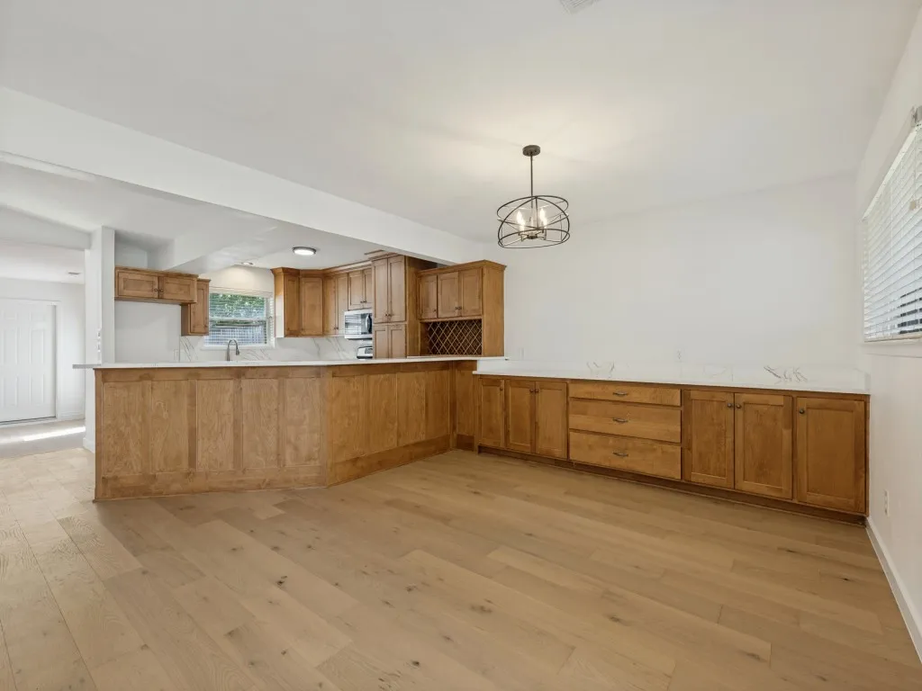 Wood-finish flooring throughout, extensive cabinetry with integrated wine rack, built-in microwave, white countertops, and a modern chandelier