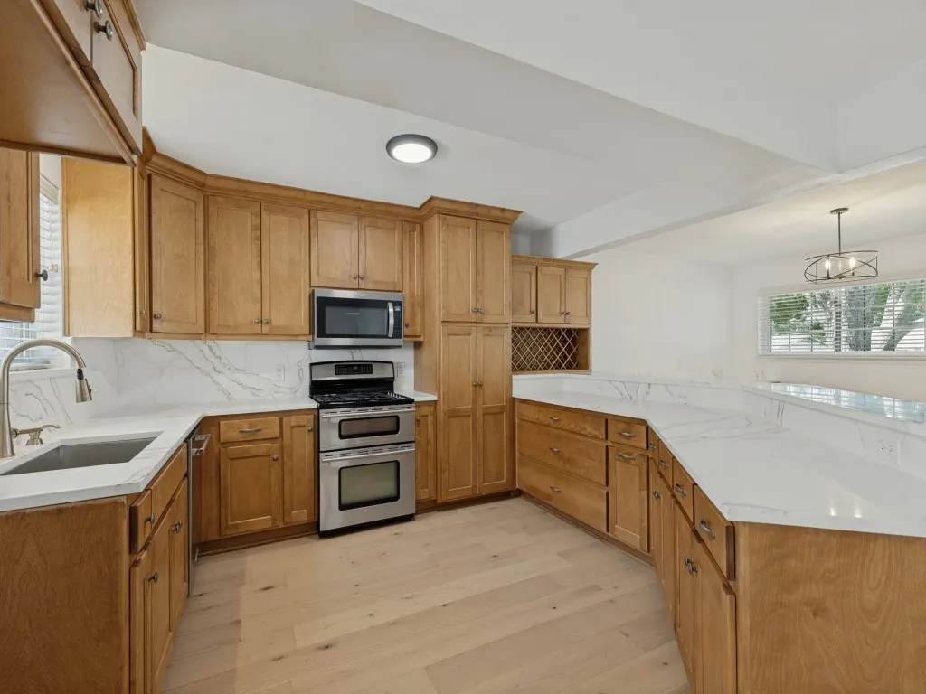 Light wood-finish cabinetry with white countertops, stainless steel appliances, and wood-finish flooring