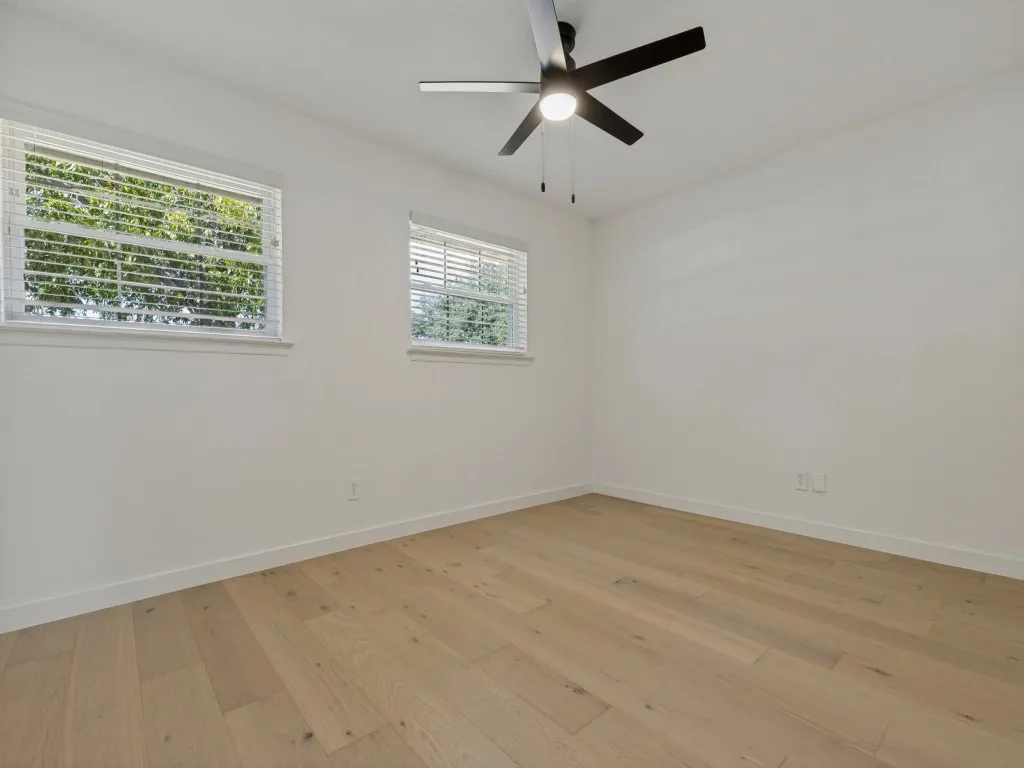 Wood-finish flooring, white walls, two windows with blinds, and a ceiling fan with integrated lighting