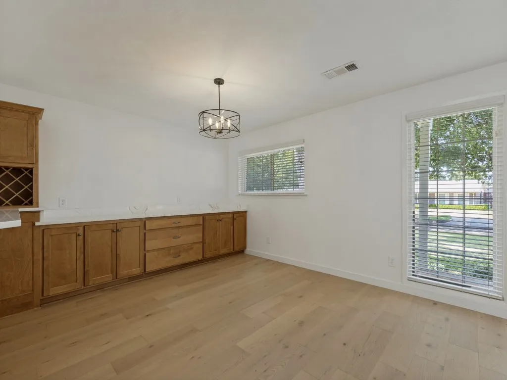 Wood-finish flooring, built-in cabinetry with white countertops, two windows with blinds, and a suspended black metal light fixture
