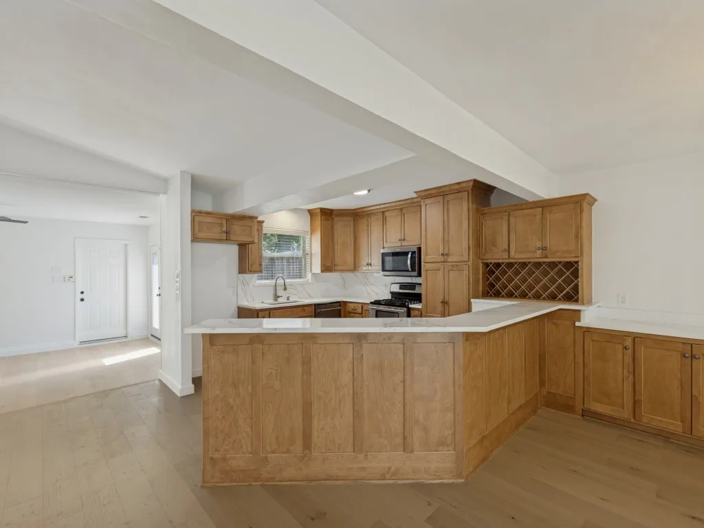 Wood-finish flooring throughout, kitchen with wood cabinetry, stainless steel appliances, white countertops, and integrated wine storage