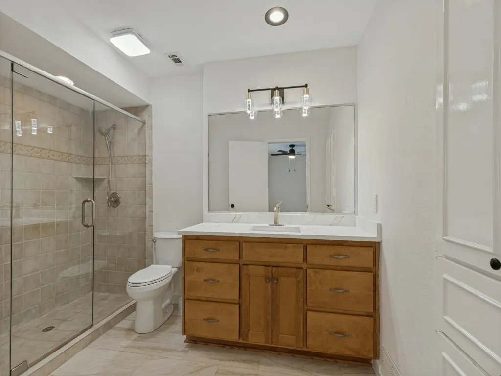 Tiled shower with glass enclosure and built-in shelf, neutral tone flooring, wood-finish vanity with countertop, and framed mirror