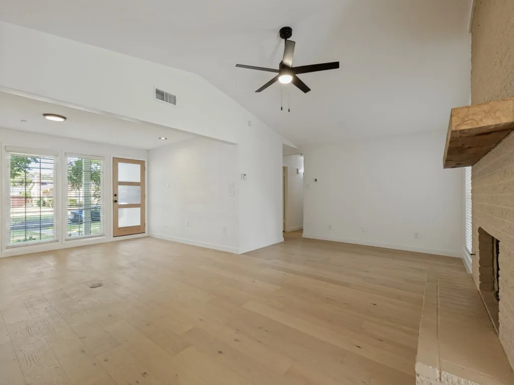 Vaulted ceiling with a ceiling fan, light wood-finish flooring, and a fireplace with a wood mantle
