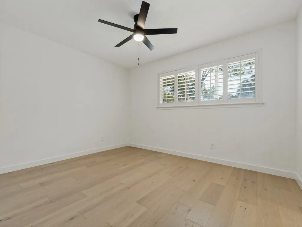 Light wood-finish flooring, white walls, and a multi-pane window with white plantation shutters