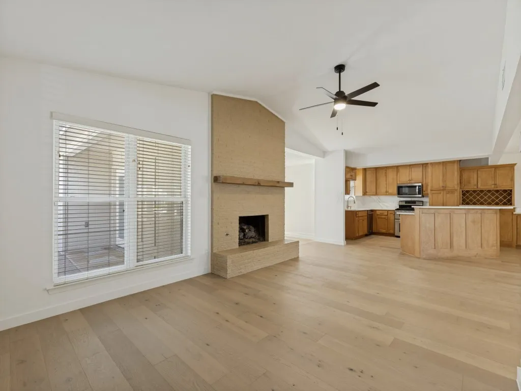 Vaulted ceiling, ceiling fan, wood-finish flooring, brick fireplace with wood mantel, and kitchen with wood cabinetry