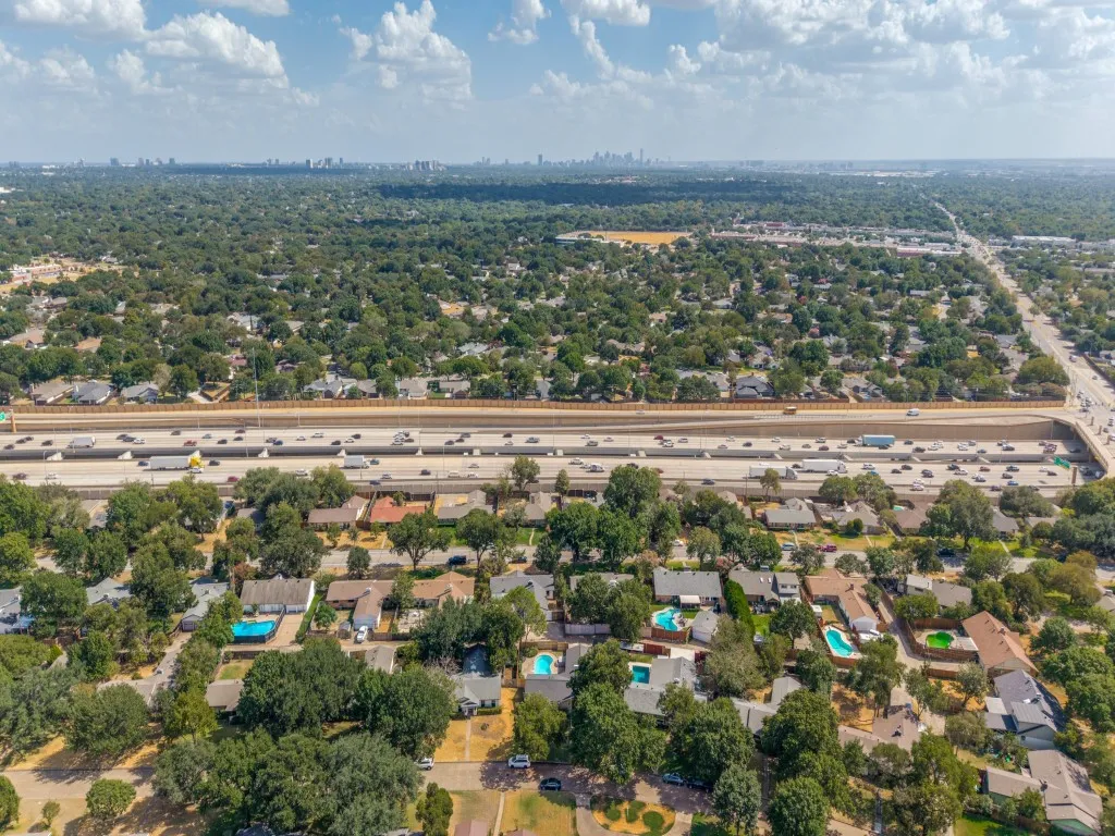 Aerial perspective showcasing an expansive residential area with abundant mature trees and multiple private swimming pools