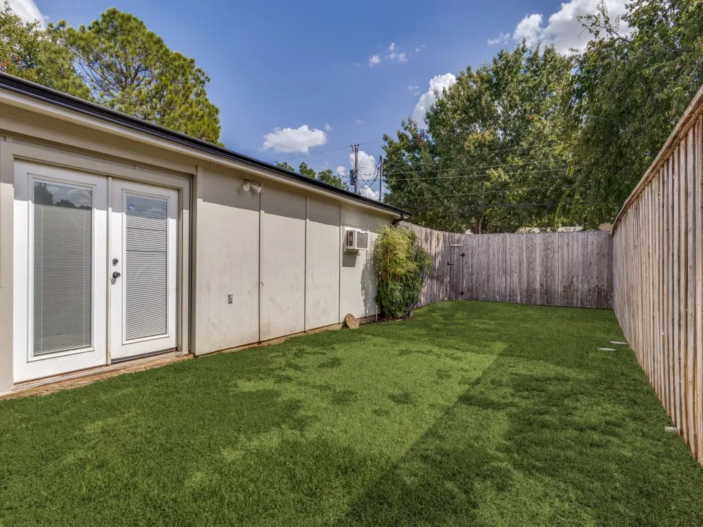 Private fenced yard with artificial turf, featuring a double glass panel door and an exterior light fixture