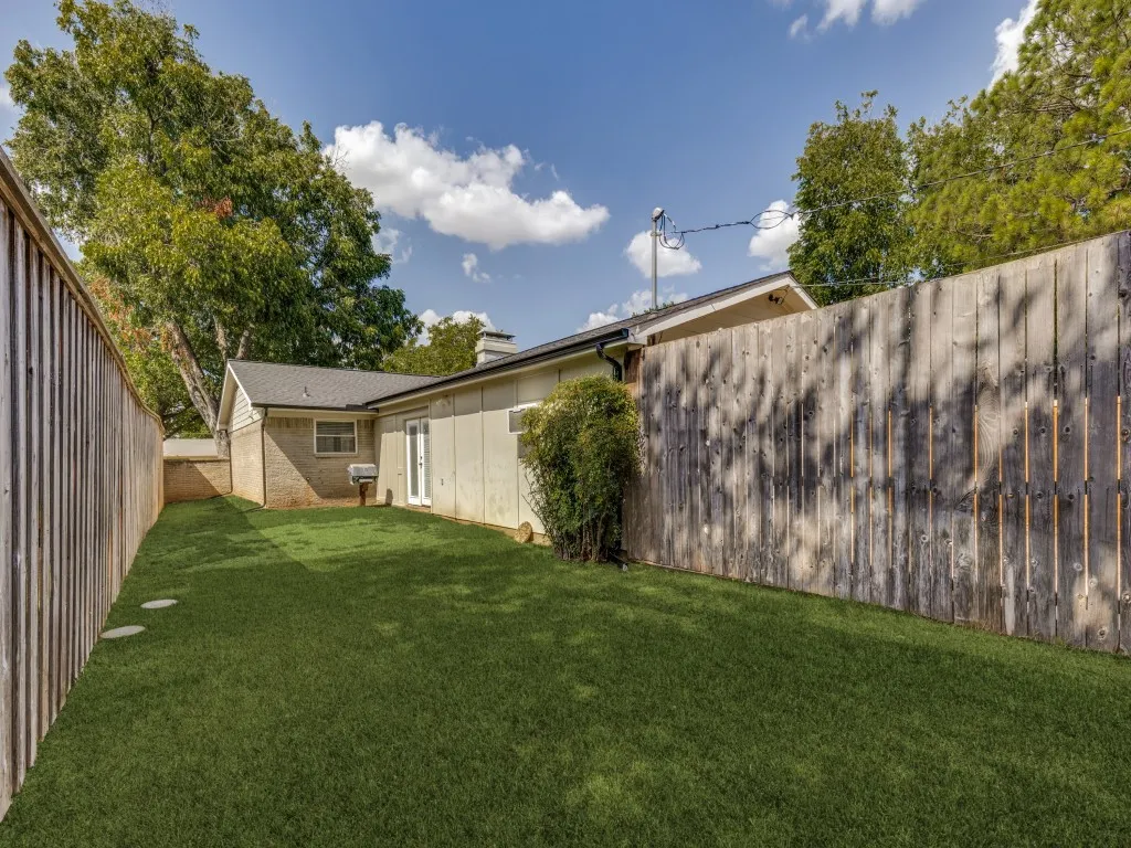 Fenced backyard featuring synthetic turf, concrete stepping stones, and a rear exterior door