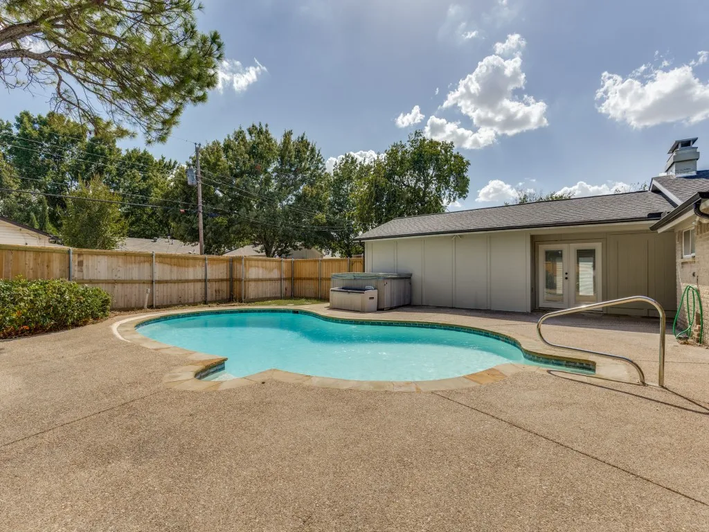 Fenced backyard featuring an in-ground swimming pool, concrete decking, and a built-in hot tub
