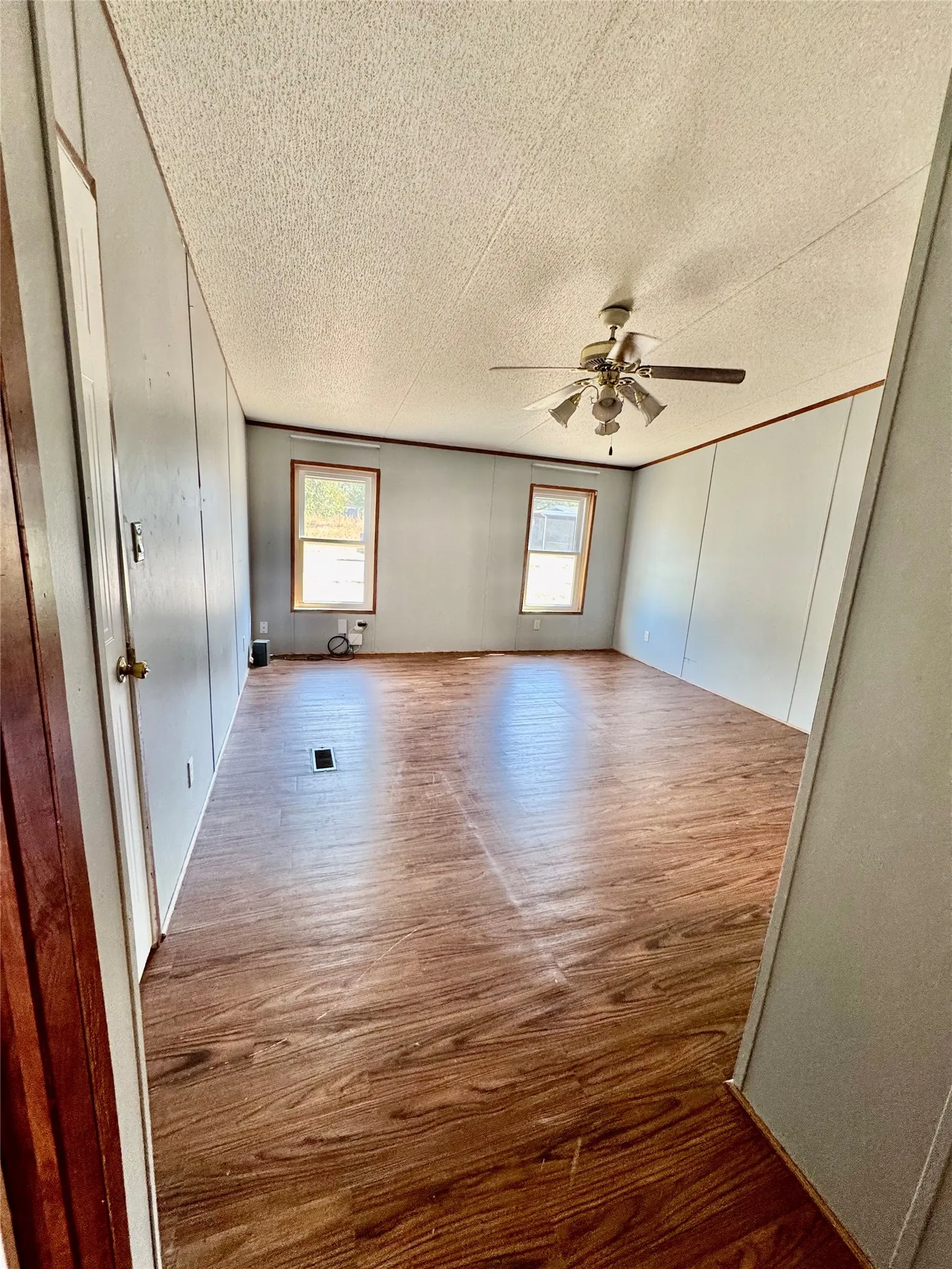 Spacious interior with wood-finish flooring, two large windows, a ceiling fan, and light-colored wall paneling