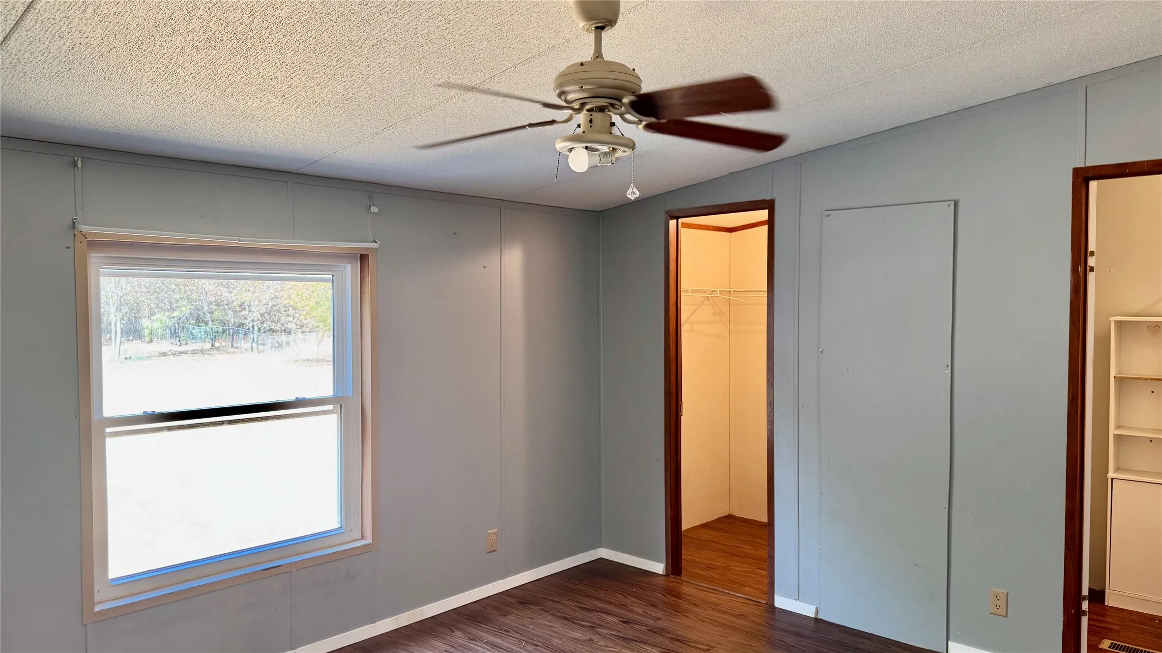 Wood-finish flooring, ceiling fan with light fixture, interior window, and two open doorways