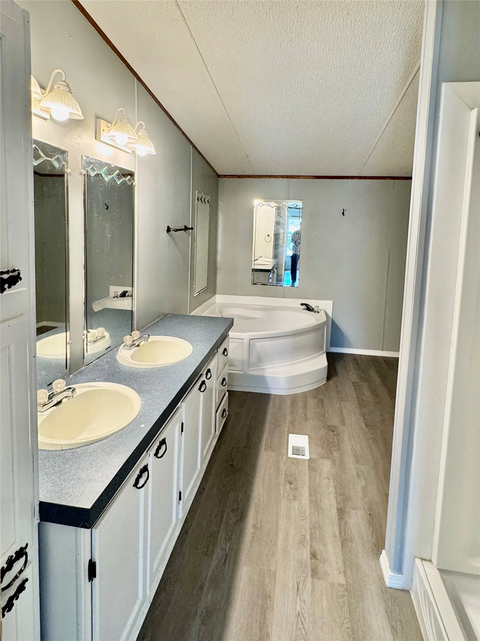Spacious bathroom featuring a dual vanity, white cabinetry, a built-in soaking tub, and wood-finish flooring
