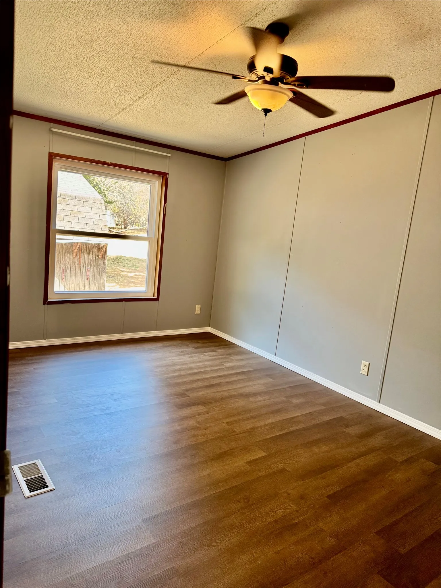 Wood-finish flooring with white trim, a fixed window, and a ceiling fan with integrated lighting