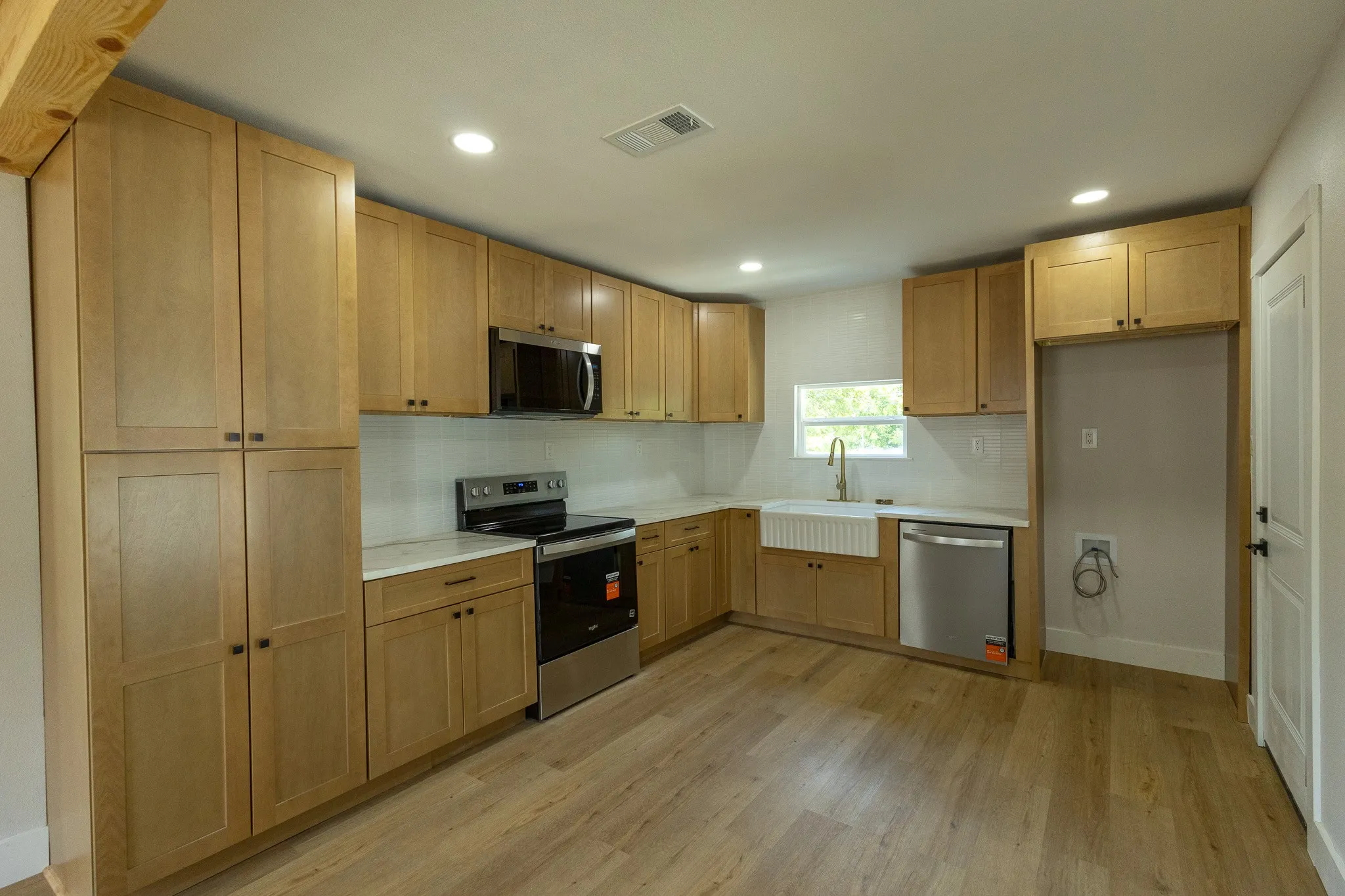 Contemporary kitchen featuring light wood-finish cabinetry, stainless steel appliances, a white farmhouse sink, and recessed lighting