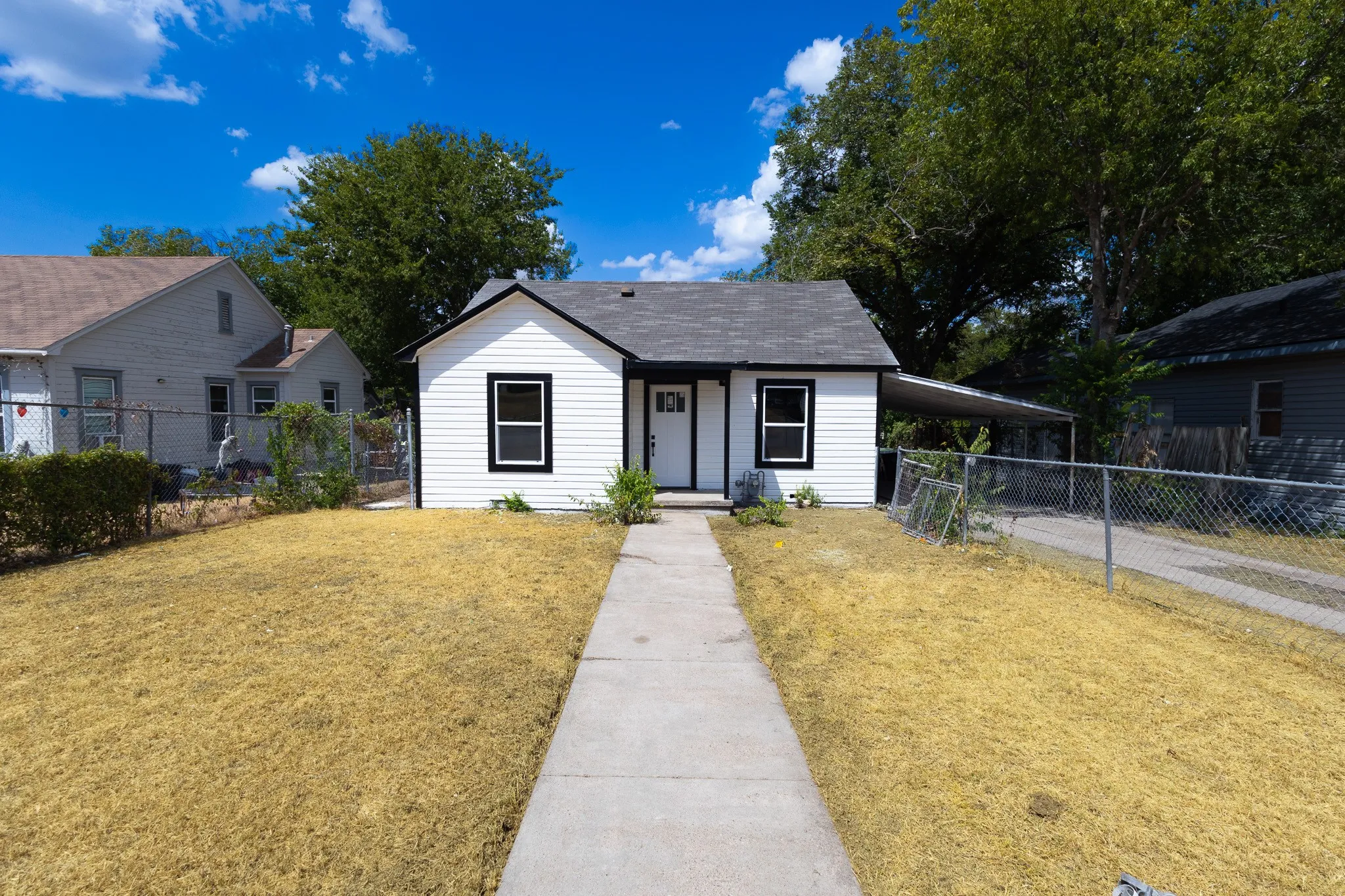 White exterior siding with black trim, a dark shingle roof, a covered carport, and a concrete walkway