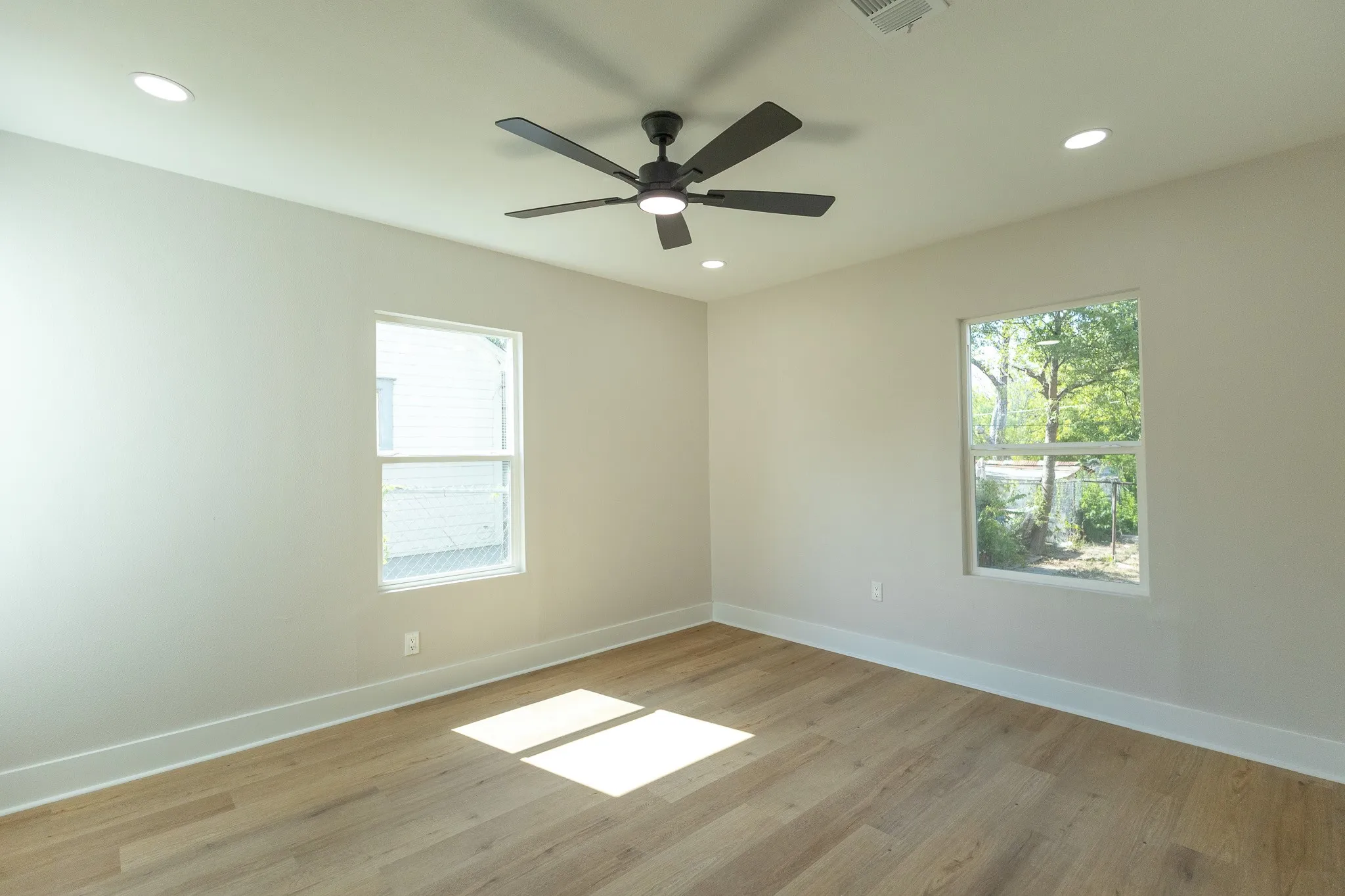 Spacious room with wood-finish flooring, recessed lighting, a ceiling fan, and multiple windows