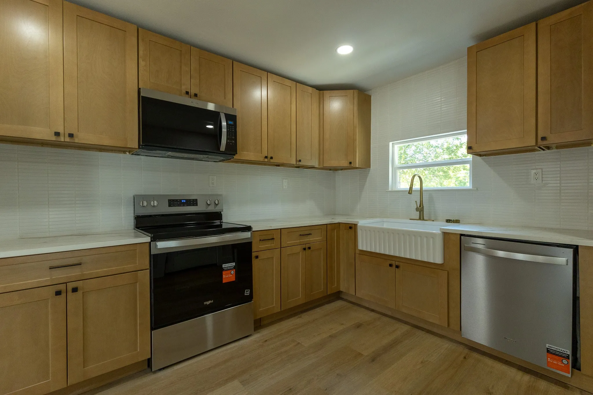 Kitchen featuring wood-finish cabinetry, stainless steel appliances, a farmhouse sink with a gold-tone faucet, and white subway tile backsplash