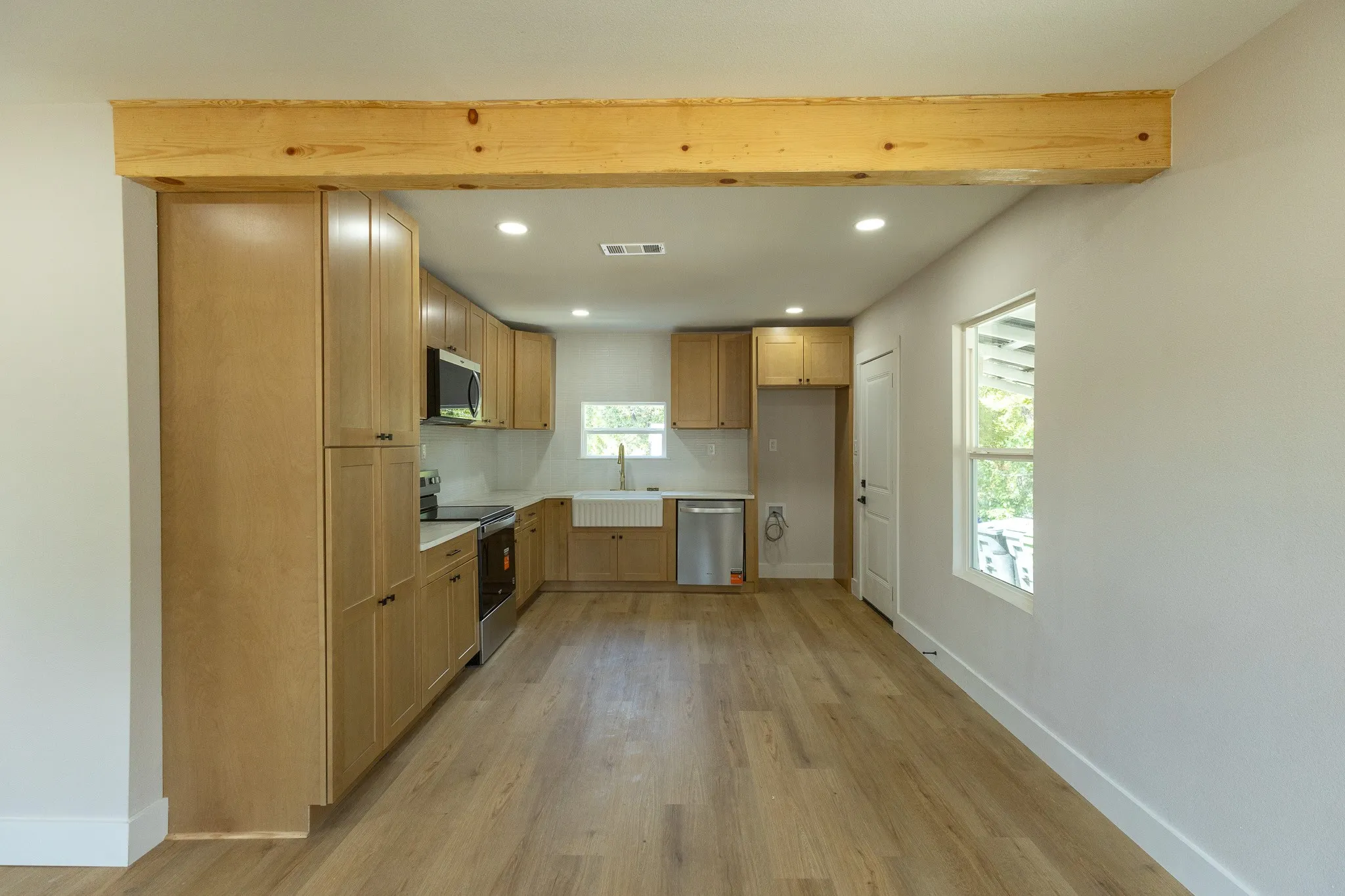 Open-concept kitchen with wood-finish flooring, light wood cabinetry, stainless steel appliances, and recessed lighting