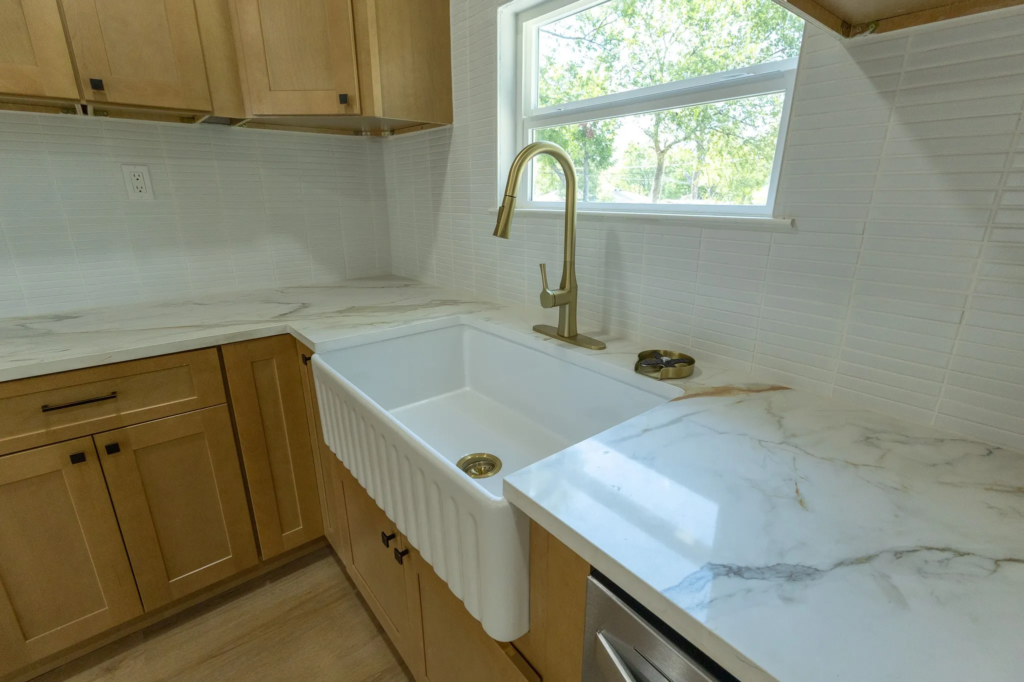 Farmhouse sink with a gold-finish gooseneck faucet, light wood-finish cabinetry, and white countertops