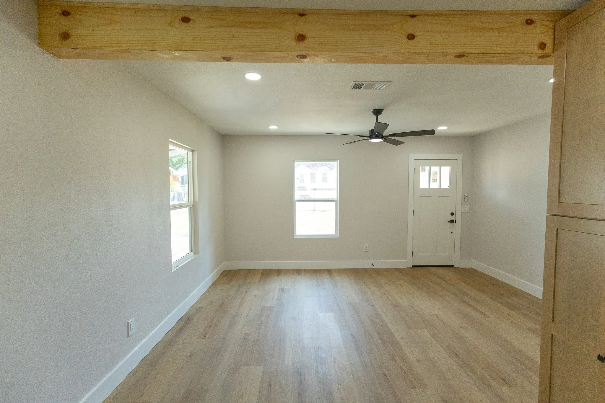 Exposed wood beam accenting the ceiling, recessed lighting, ceiling fan, wood-finish flooring, and a white paneled entry door