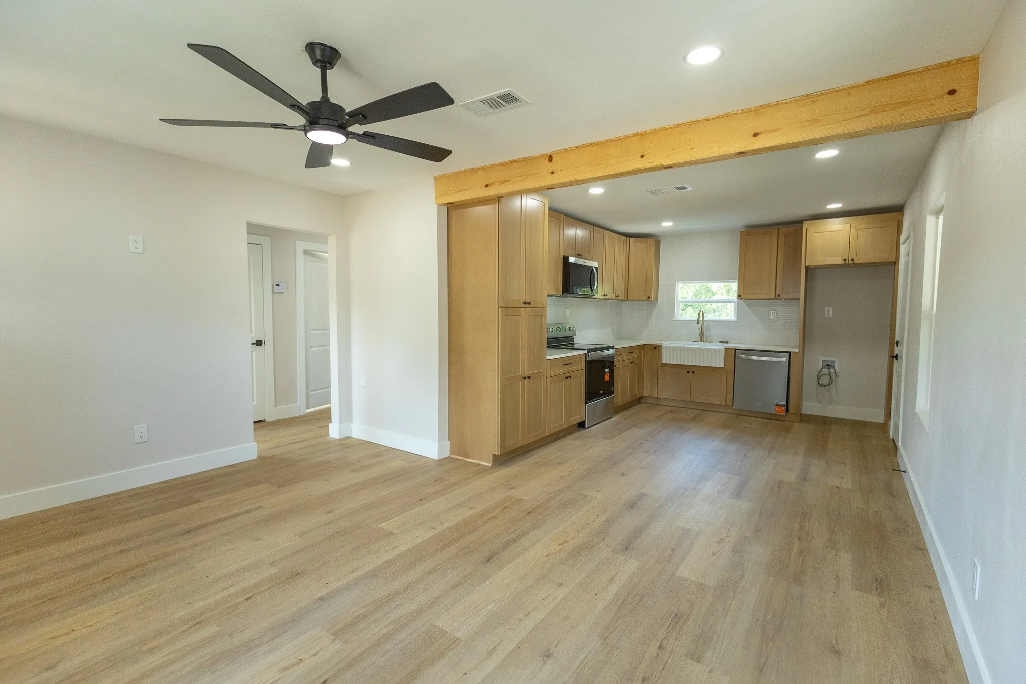 Open-concept living space featuring wood-finish flooring, a modern ceiling fan, recessed lighting, and a kitchen with wood cabinetry and a farmhouse sink