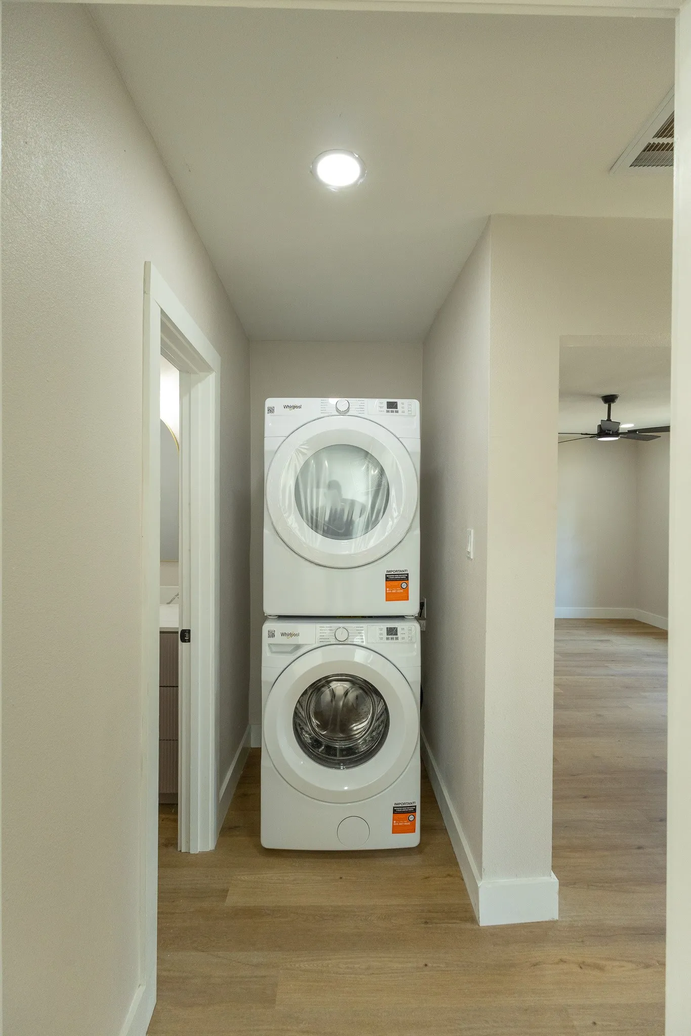 Stacked washer and dryer unit, wood-finish flooring, recessed lighting, and a ceiling fan visible in the background