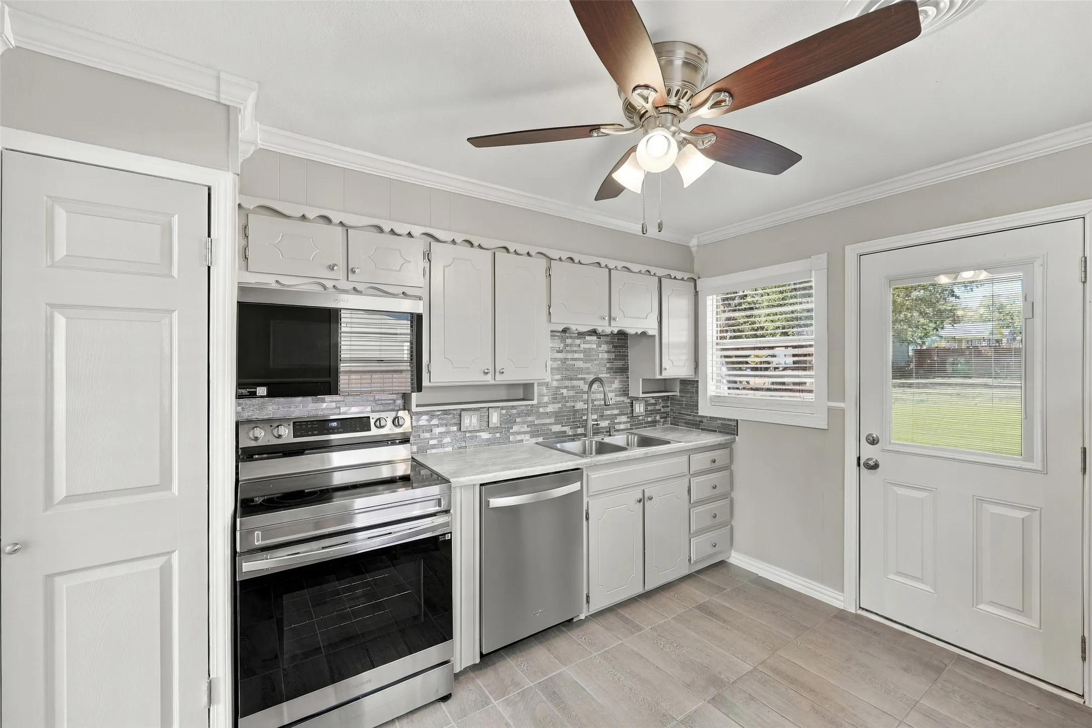 Kitchen featuring stainless steel appliances, white cabinetry, tile backsplash, wood-finish flooring, and a ceiling fan