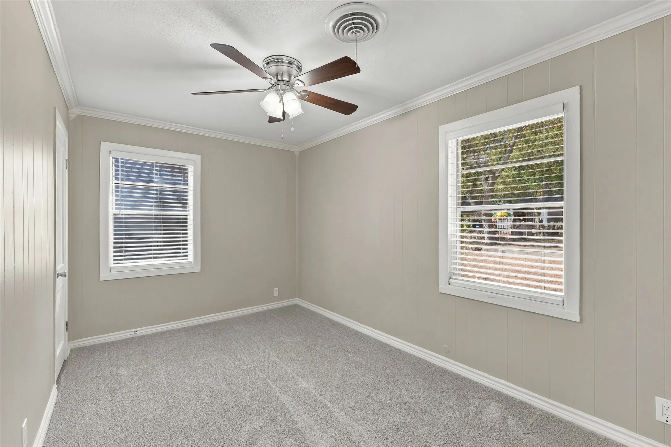 Carpeted room featuring two windows, crown molding, and a ceiling fan with integrated lighting