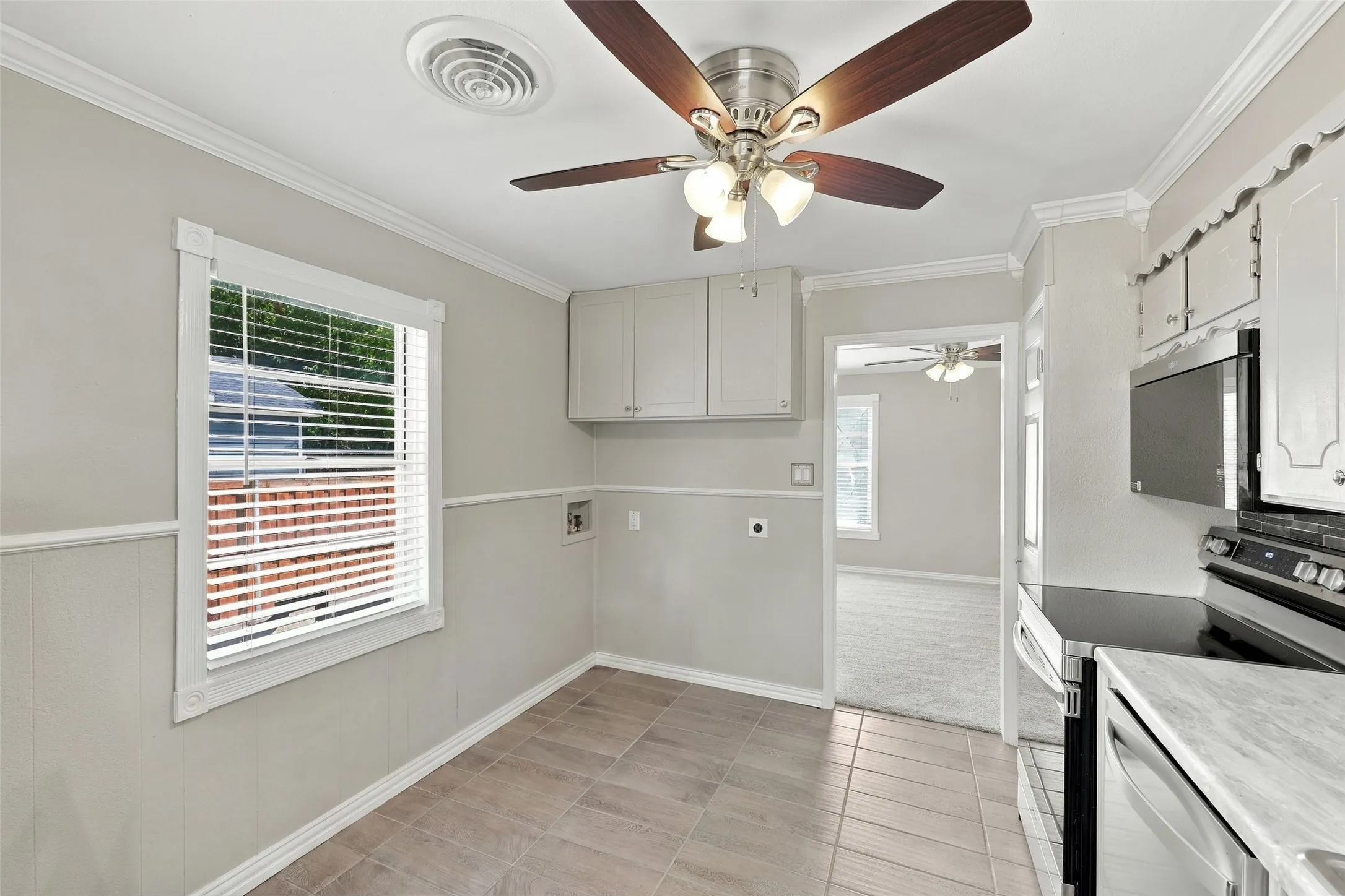 Kitchen featuring tile flooring, white cabinetry, stainless steel microwave, and a ceiling fan with integrated lighting