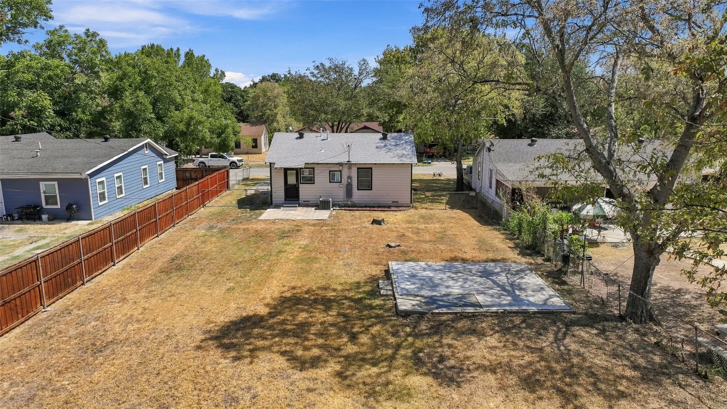 Expansive backyard featuring a privacy fence, mature trees, and a concrete patio