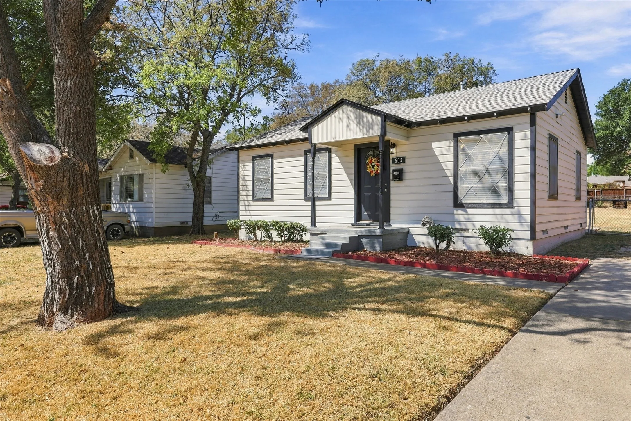 White siding exterior with dark trim accents, covered front entry, concrete walkway, and mature trees