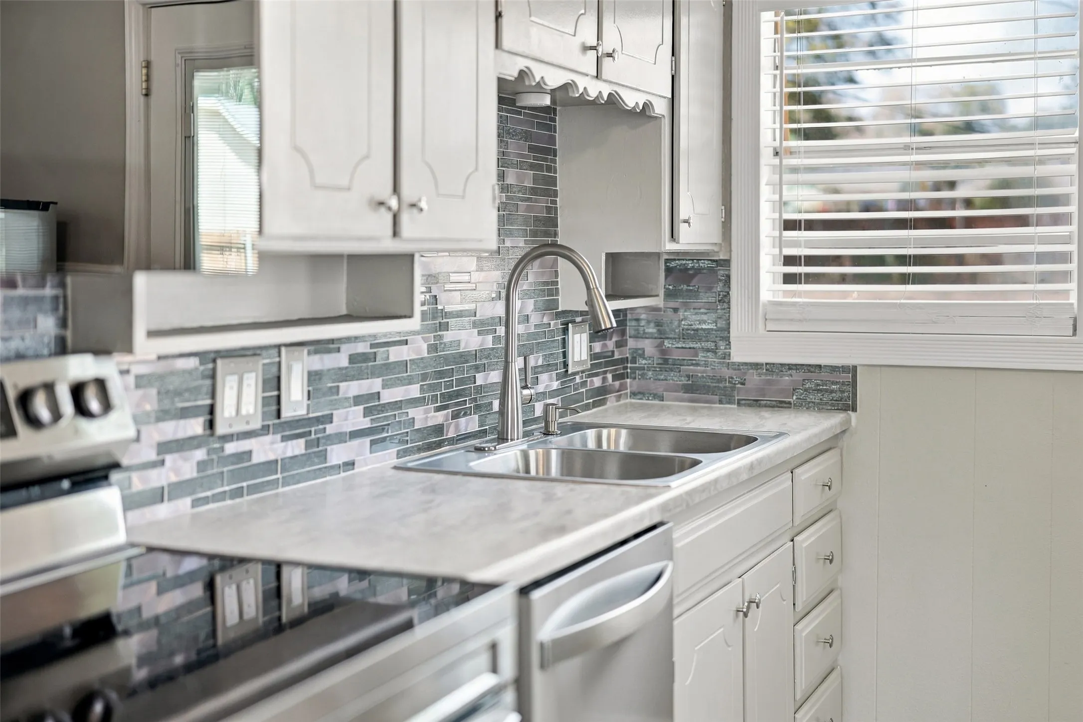White cabinetry, dual-basin stainless steel sink, and patterned tile backsplash