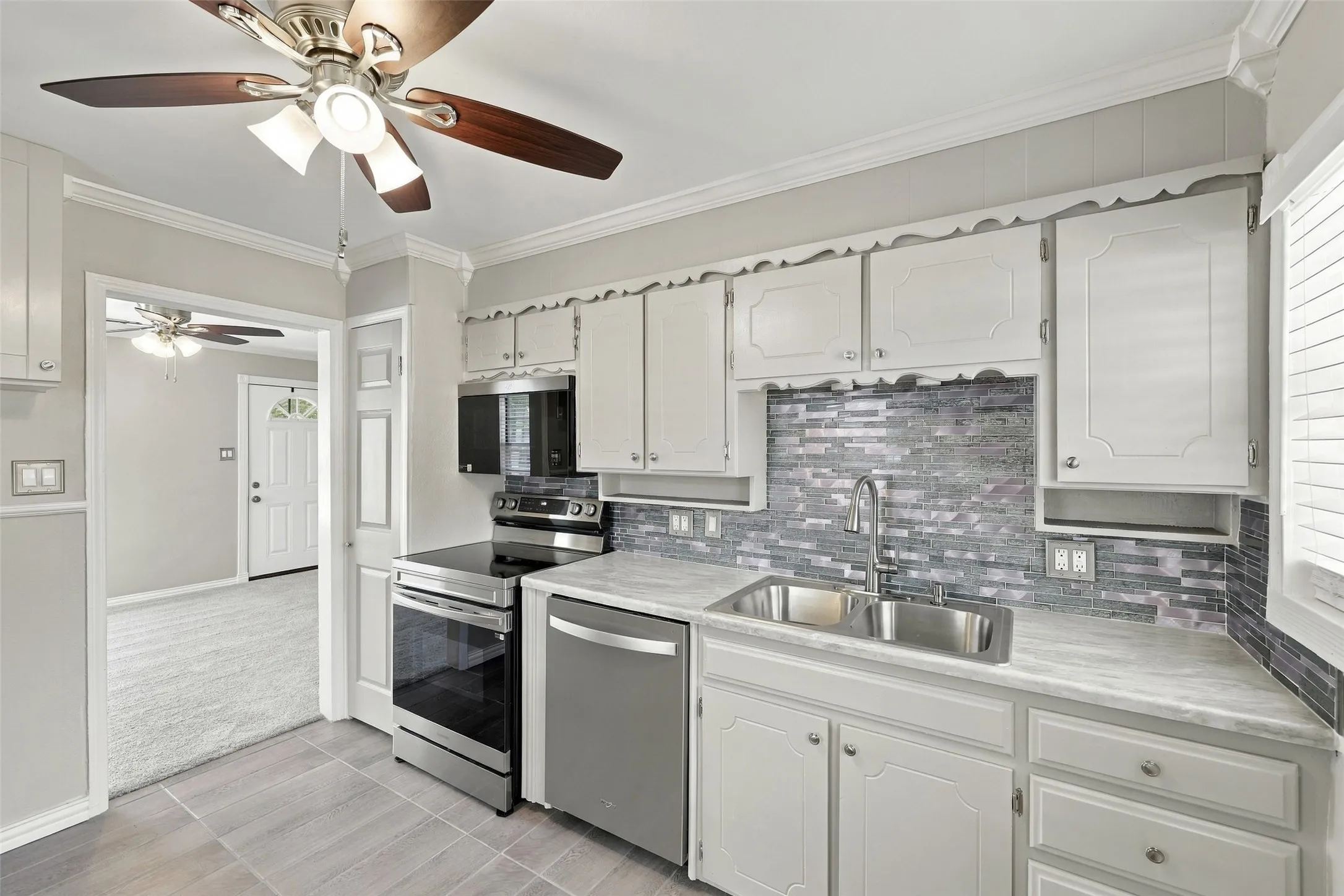 White cabinetry with crown molding, stainless steel appliances, stone-look countertops, and a mosaic tile backsplash