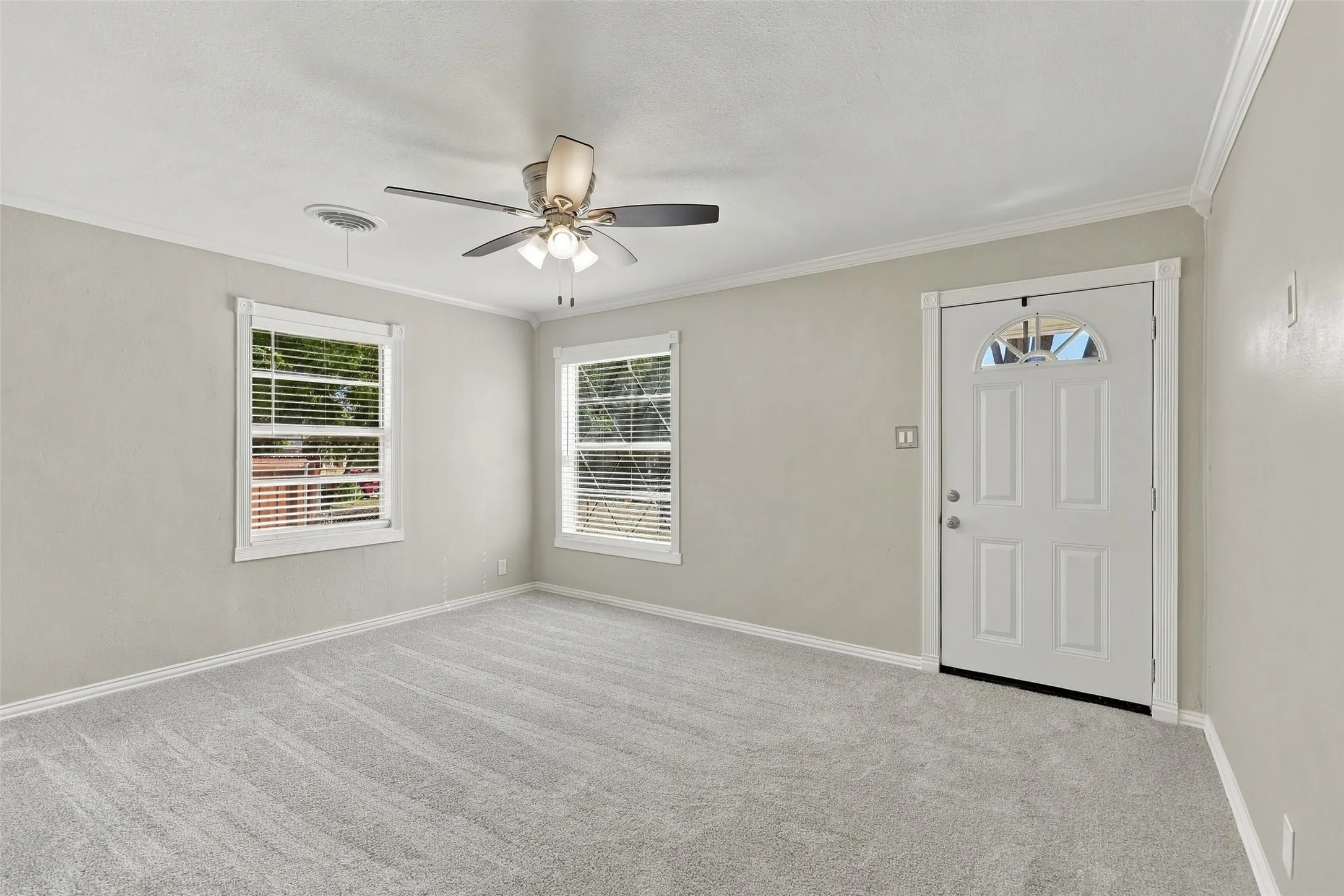 Light gray wall paint, two windows with blinds, a ceiling fan with integrated lighting, and a white paneled entry door with an arched glass insert