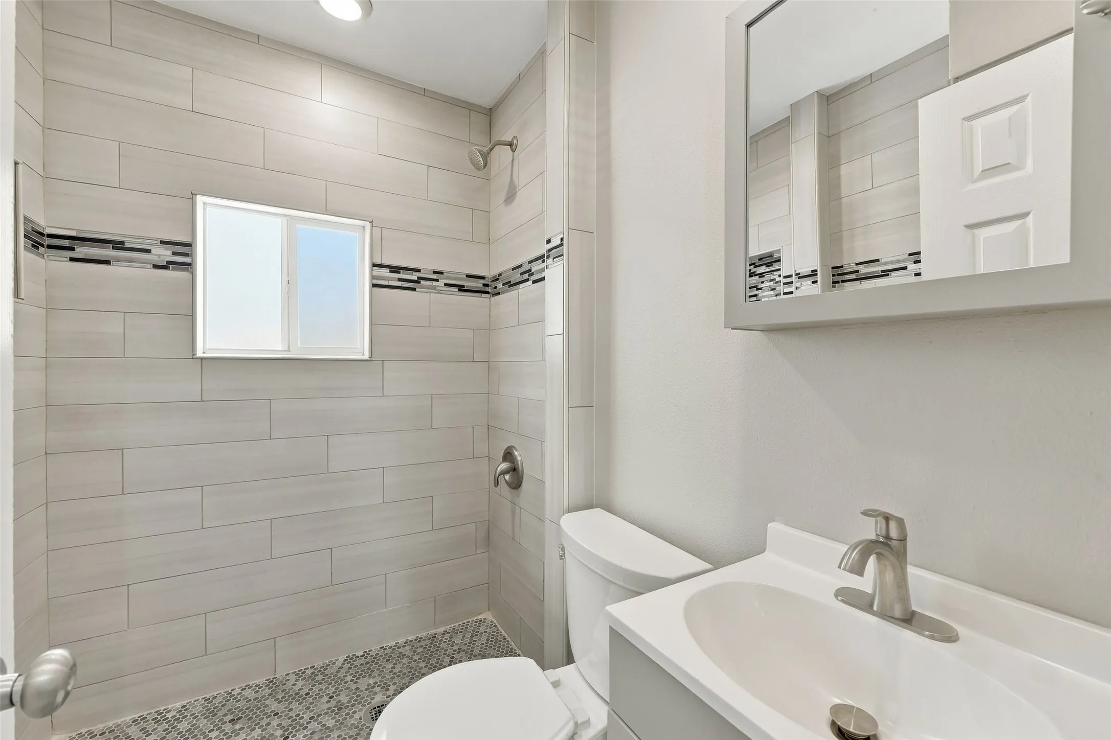 Shower with light gray rectangular tile, mosaic accent tile, and pebble flooring