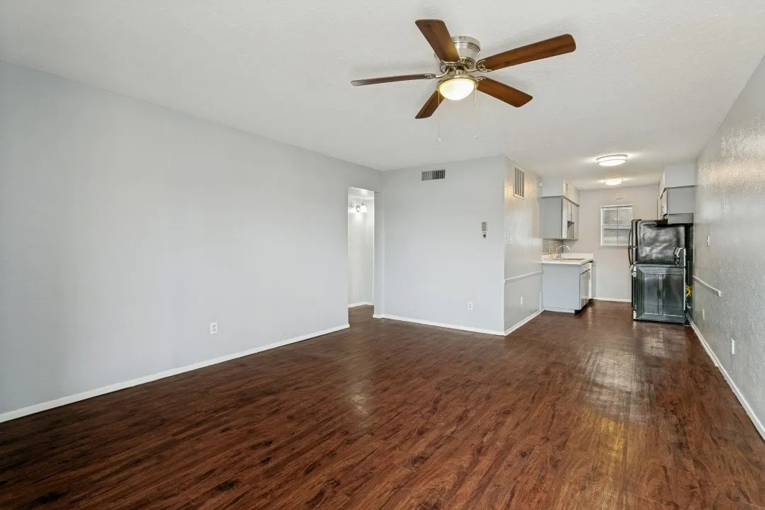 Wood-finish flooring throughout, ceiling fan with integrated lighting, recessed lighting in the kitchen, light gray cabinetry, and a black refrigerator